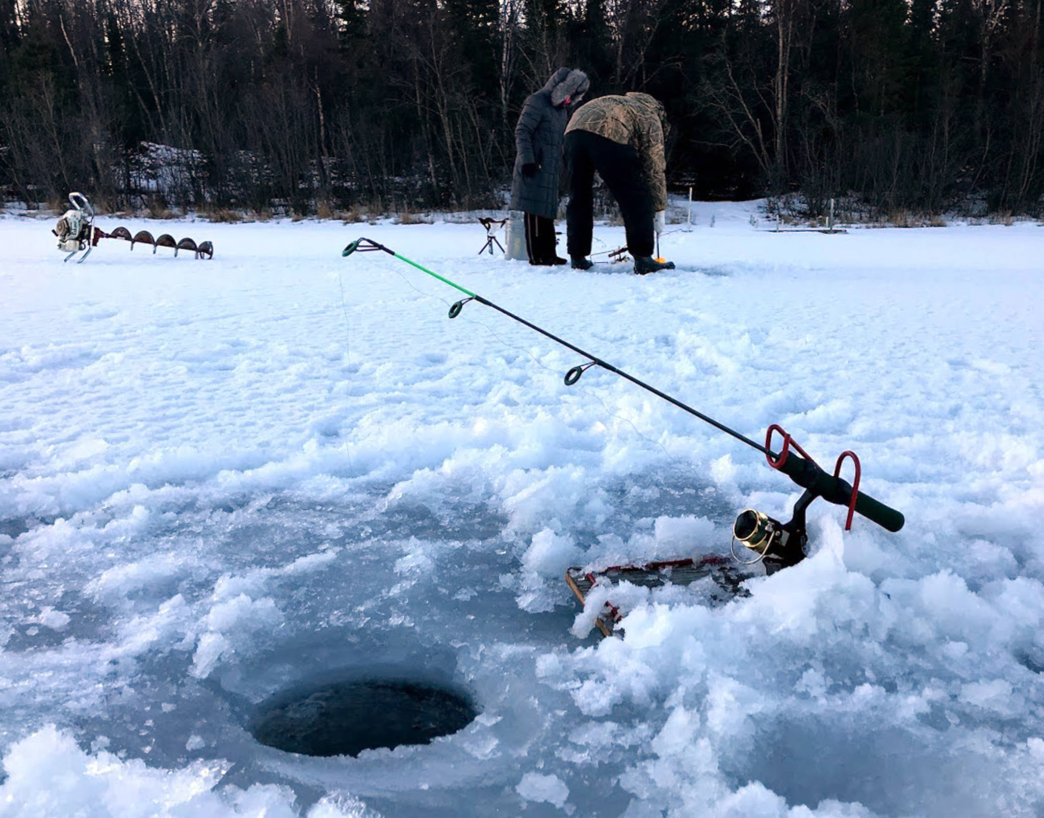 Some of the tools for ice fishing, including a rod, holder and auger, are seen here during a trip fishing on Spirit Lake Dec. 26, 2017, while other anglers continue to set up their rigs to fish. (Photo by Kat Sorensen/Peninsula Clarion)