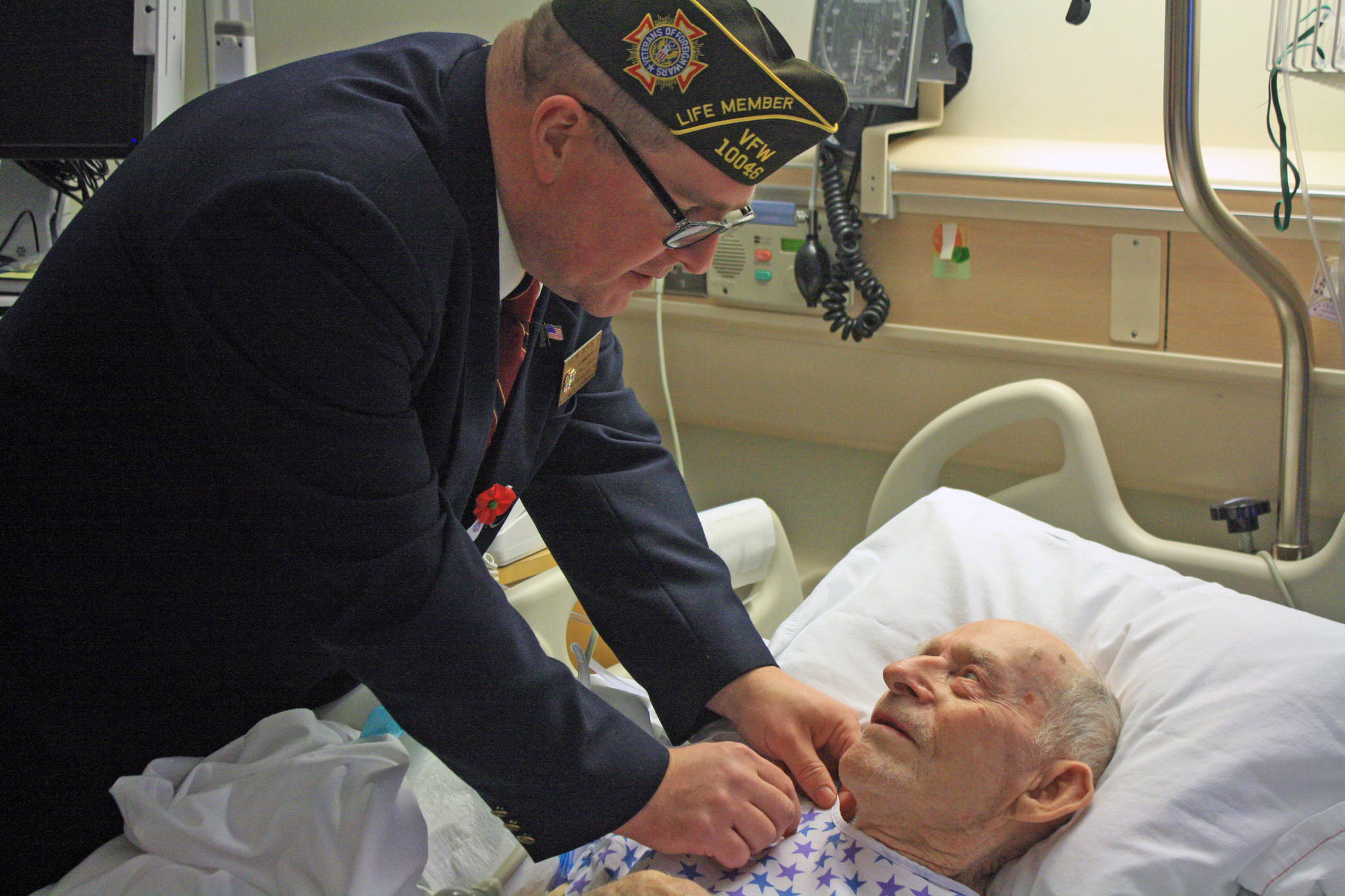Soldotna VFW Commander John Walker attaches a 70-year service pin to World War II veteran Bill Field at the Central Peninsula Hospital on Monday. (Photo by Erin Thompson/Peninsula Clarion)