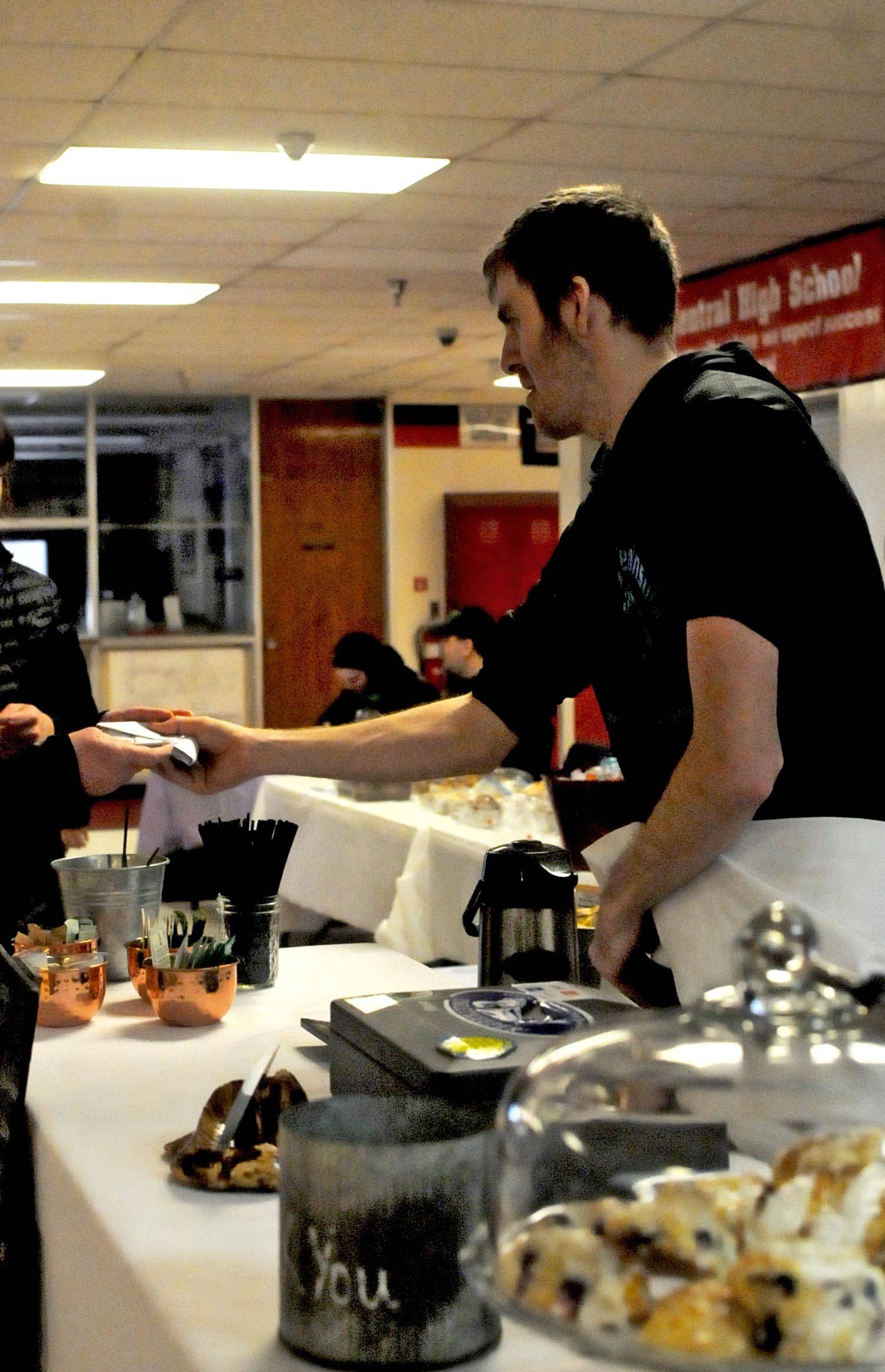 Tony Kaser helps a customer at the Hearth Eathery and Catering’s stand during a craft fair fundraiser for the Central Peninsula Special Olympics at Kenai Central High School on Saturday, March 3, 2018 in Kenai, Alaska. The fair featured a number of artists and craftsmen selling work ranging from paintings to wooden toys to essential oils, with proceeds from the fair going to assist the Special Olympics in purchasing jerseys, equipment, transportation and training costs. The Central Peninsula Special Olympics coordinates sports programs for people with intellectual disabilities as a subprogram of the statewide Special Olympics. Kaser participates in swimming in the Special Olympics. (Photo by Elizabeth Earl/Peninsula Clarion)