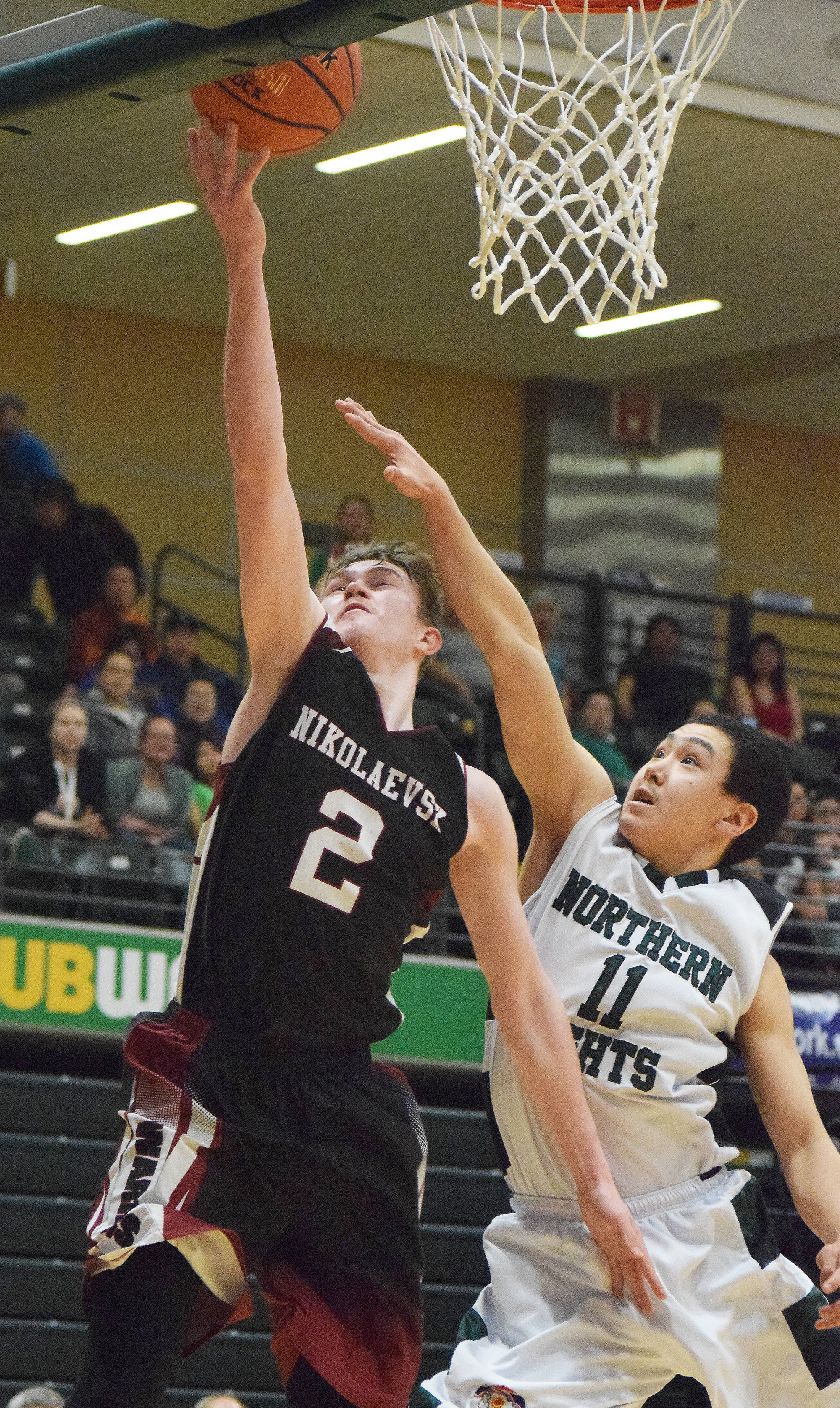 Nikolaevsk’s Kalenik Molodih (2) lays in a bucket against Shishmaref’s Fred Sinnok Friday in a Class 1A state tournament fourth-place semifinal contest at the Alaska Airlines Center. (Photo by Joey Klecka/Peninsula Clarion)