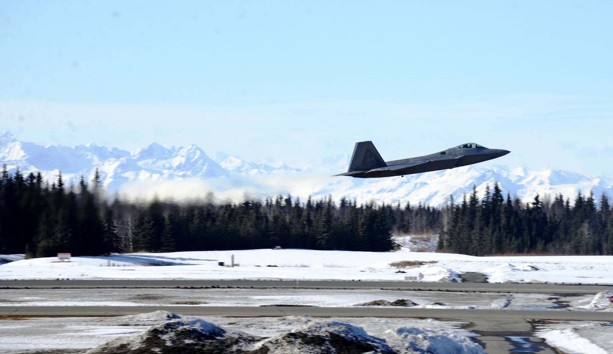 As a U.S. Air Force F-22 “Raptor” fighter jet takes off from the Kenai Municipal Airport, others await fueling on Monday, March 19, 2018 in Kenai. Eight of the fighters landed at the Kenai airport Monday after weather conditions kept them from Joint Base Elmendorf-Richardson in Anchorage, their home field. Four of the F-22s belong to the 90th Fighter Squadron and four to the 525th Fighter Squadron, which were on separate training flights before landing in Kenai, said Major Stephen Montgomery, a pilot with the 90th. The fighters took off for Anchorage Monday afternoon. F-22s from Elmendorf have been occasionally using Kenai as an alternate landing site since October 2016, when a pair of the fighters landed there to assess the possibility. (Photo by Ben Boettger/Peninsula Clarion)