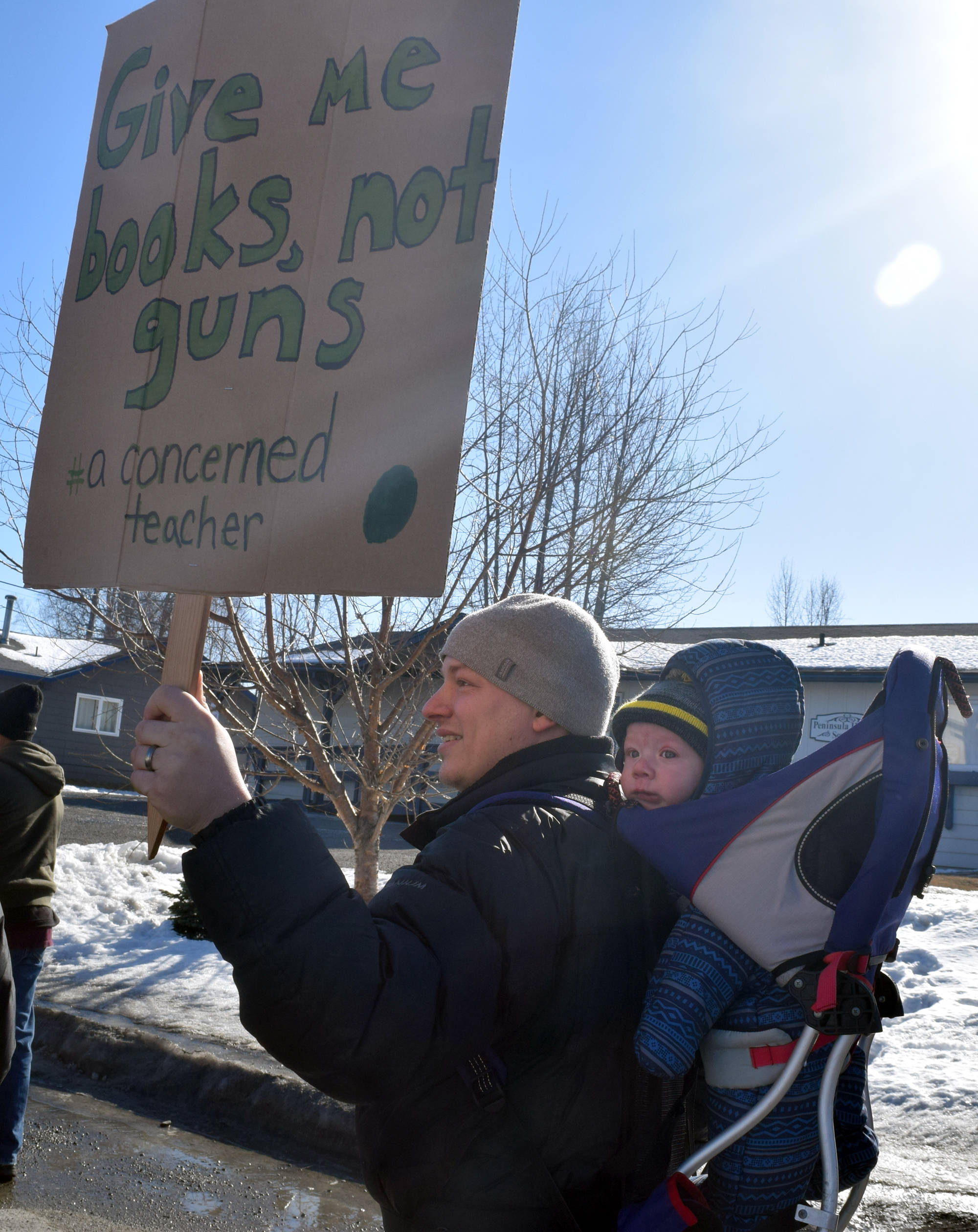 Daniel Bowen walks along North Binkley Street with his son Zachary on his back to the Kenai Peninsula Borough building in Soldotna on Saturday as part of the national March for Our Lives rally, which took place in cities and towns across the country in support of gun control laws. (Photo by Kat Sorensen/Peninsula Clarion)