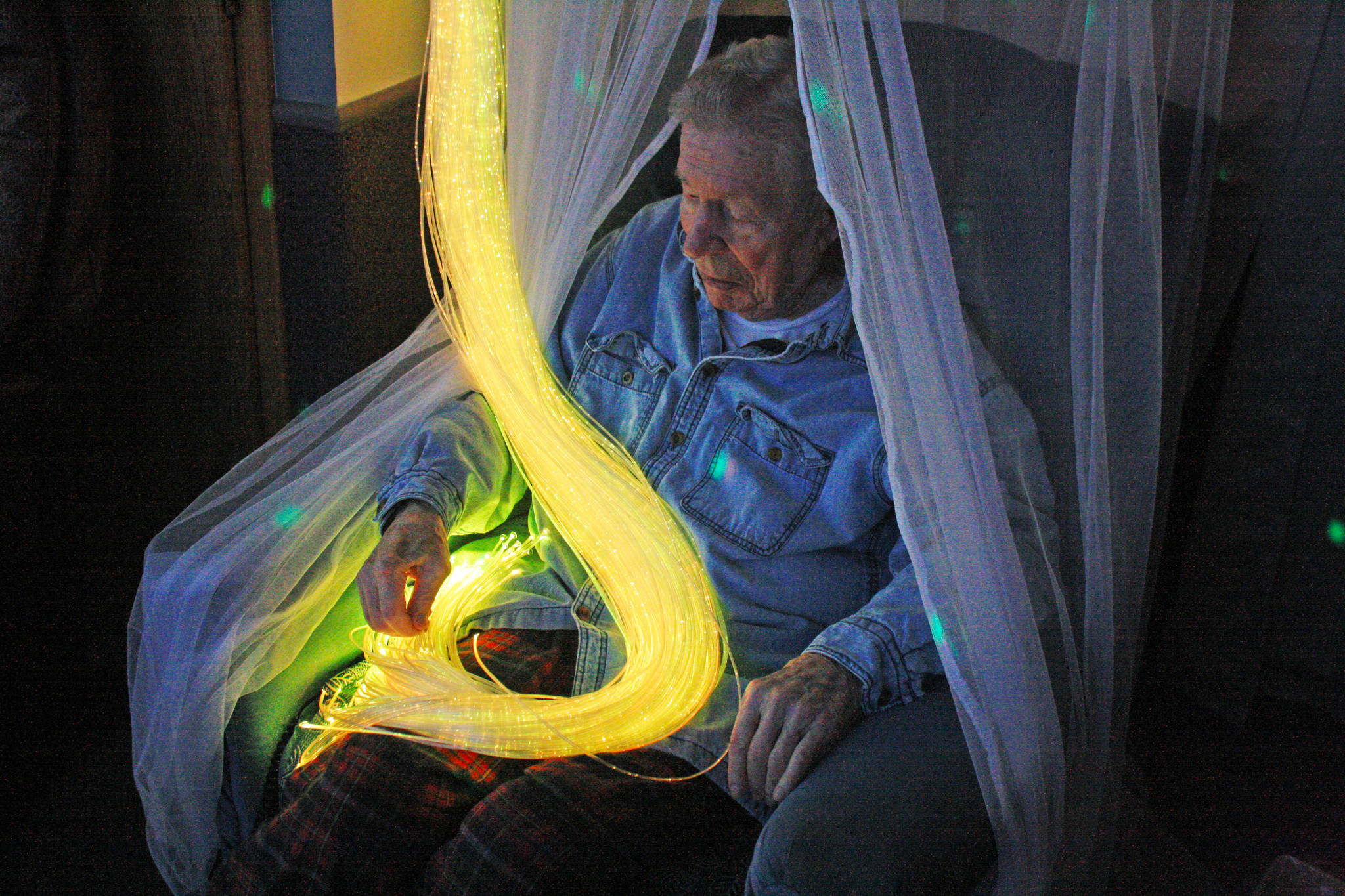 A resident at Heritage Place enjoys colored strands of light during an open house of the home’s Snoezelen room on Friday, March 23 in Soldotna. (Photo by Erin Thompson/Peninsula Clarion)