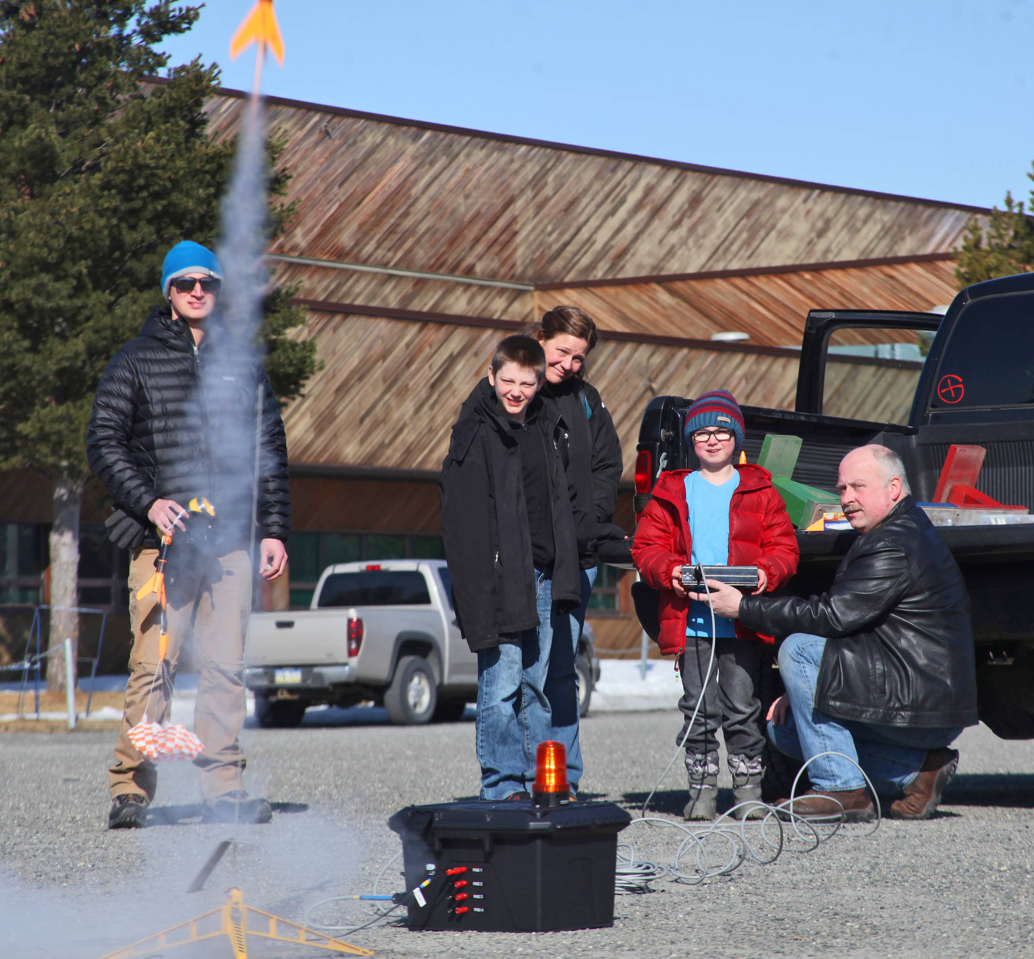 With the push of a button, Owen Walsh (in red) sends a model rocket into the sky, as instructor Scott Aleckson (right) and other students of his rocketry class watch in the parking lot of the Soldotna Regional Sports Complex in Soldotna, Alaska on Saturday, May 31, 2018. Aleckson said he made and launched his first plastic, balsa wood, and cardboard rocket as a 4th grade student at Soldotna Elementary School. Since then he’s built a custom launch system, he said, “with recycled electronics and a lot of soldering time.” Aleckson taught Saturday’s rocketry class through the Soldotna Community Schools program, and would like to continue spreading the hobby. “If I could get a model rocket club going, that’d be great,” he said. “Stuff like this is much more fun in a group.” (Photo by Ben Boettger/Peninsula Clarion)