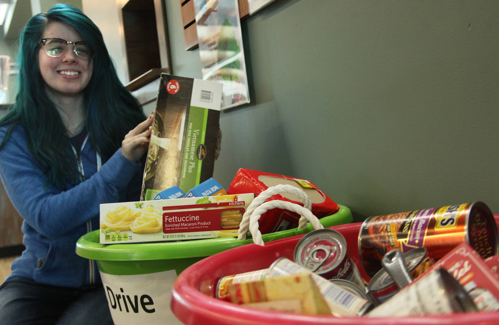 Youth Librarian Ali Jobe of the Joyce K. Carver Memorial Soldotna Public Library sits beside the canned goods and other nonperishable food items that library patrons have donated to the Kenai Peninsula Food Bank in lieu of late fees during the library’s food for fines collection drive on Wednesday, April 11, 2018 in Soldotna, Alaska. In addition to the two and a half bins of food at the library entrance, the Food Bank has already recieved 193 pounds of food since the library began collecting on April 9. Soldotna librarians will take food for fines — at an exchange rate of $1 per item — until April 14. (Ben Boettger/Peninsula Clarion).