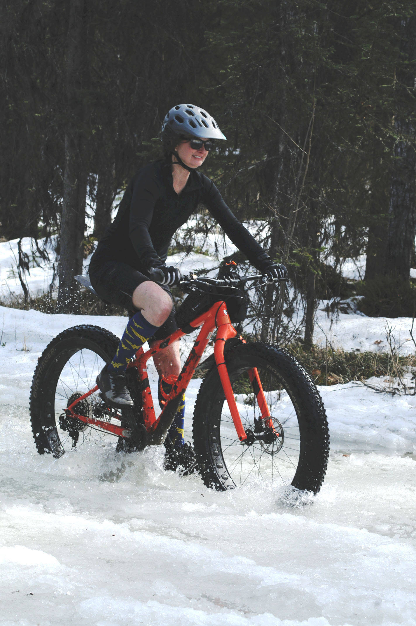 Jen Showalter of Kenai navigates her fatbike through a deep icy puddle on the Wolverine Trail during the 2018 Choose Your Weapon race at Tsalteshi Trails on Sunday, April 15, 2018 in Soldotna, Alaska. Racers completed two 5-kilometer laps around the lower trails by running, biking or skiing, with the option of switching between laps for extra points. Most of the trails had some snow with patches of wet mud sprinkled throughout as spring temperatures begin to dominate the central Kenai Peninsula. (Photo by Elizabeth Earl/Peninsula Clarion)