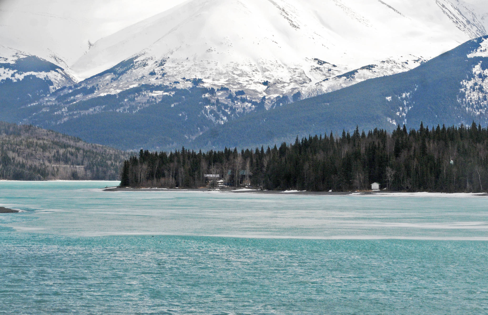 The mountains form the backdrop for Kenai Lake, which is still partially frozen, on Wednesday, April 11, 2018 seen from the bridge in Cooper Landing, Alaska. The Alaska Department of Environmental Conservation on Saturday cleaned up a small spill left over from a truck accident in February near the shore of the lake alongside the Sterling Highway. (Photo by Elizabeth Earl/Peninsula Clarion)