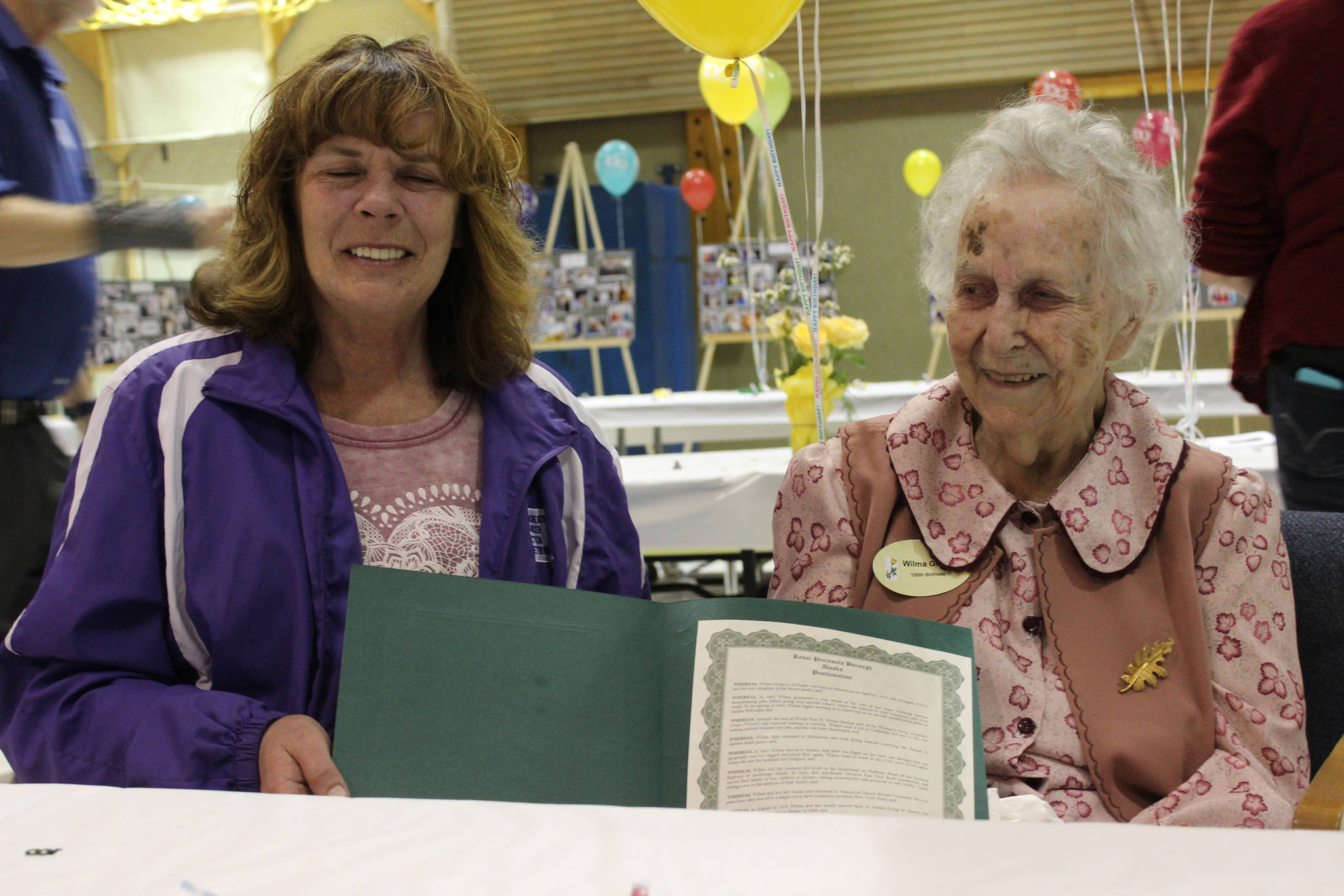 Kenai Peninsula Borough Assembly President Kelly Cooper, left, of Homer presents Wilma Gregory, right, of Homer with a borough proclamation naming Saturday Wilma Gregory Day in honor of Gregory’s 100th birthday. Friends and family celebrated with Gregory at a birthday party held at McNeil Canyon Elementary School. (Photo by McKibben Jackinsky)