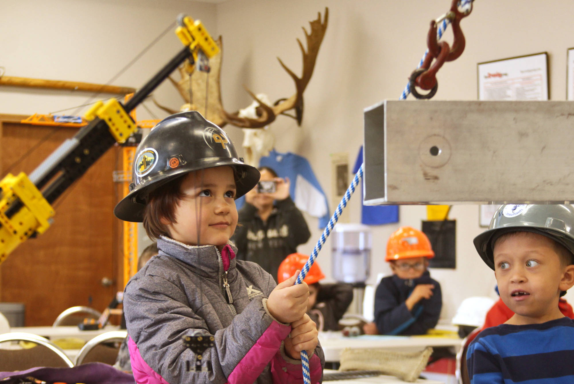 Kalifornsky Beach Elementary first-graders Melanie Partridge (left) and Aidan Gilliam serve as tagline holders, steadying a beam being lifted by a shop crane during their class’ field trip to Alaska Crane Consultants on Monday, May 7, 2018 on Kalifornsky Beach road. (Ben Boettger/Peninsula Clarion)