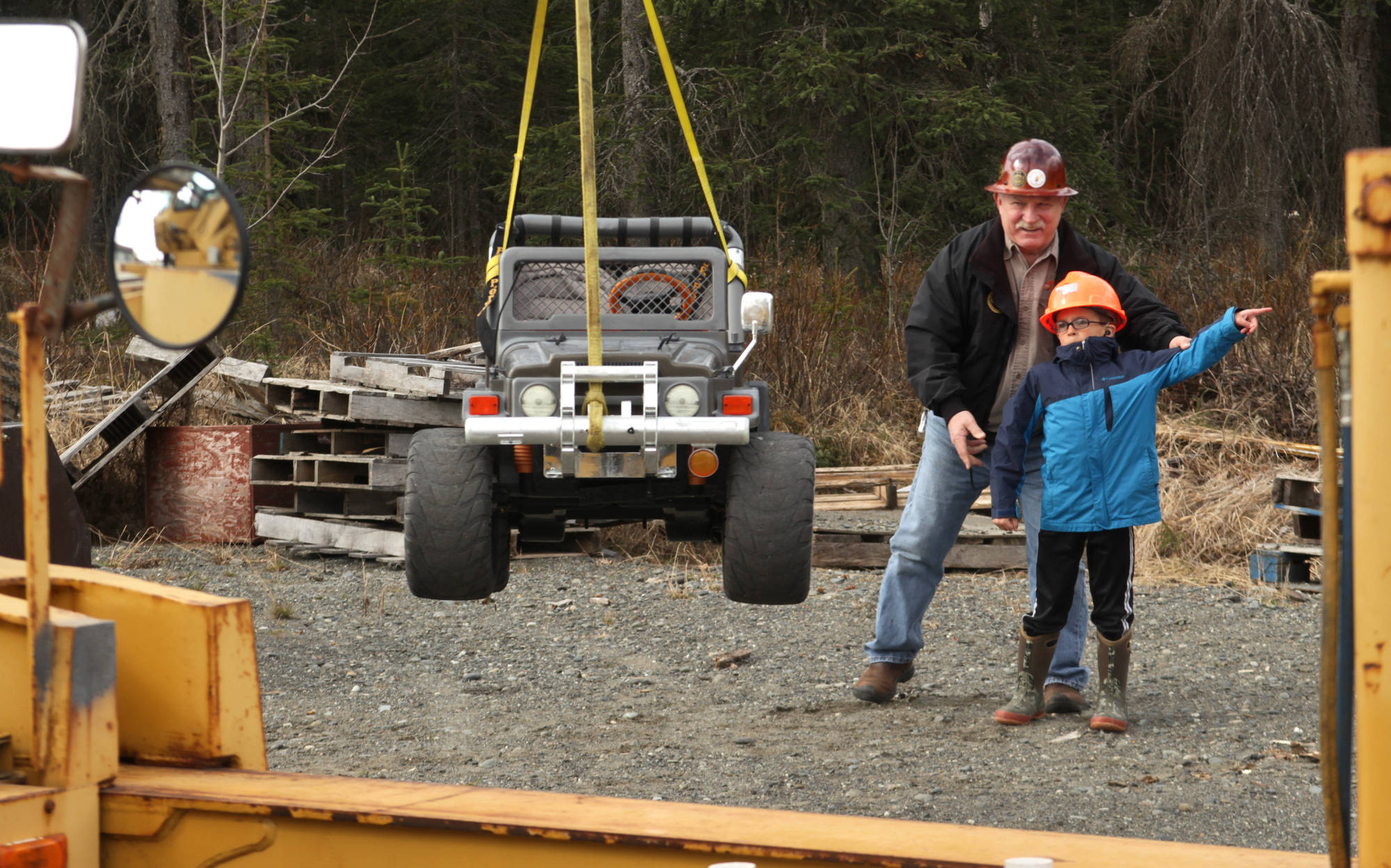 Peninsula Crane Consultants owner Bob Elmore guides Kalifornsky Beach Elementary first-grader Caleb Holper in giving hand signals to a fellow student moving a toy electric jeep with a crane during a field trip to Alaska Crane Consultants on Monday, May 7, 2018 on Kalifornsky Beach road. (Ben Boettger/Peninsula Clarion)