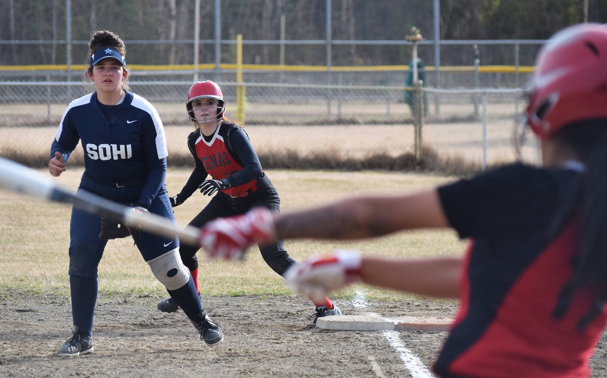 Kenai’s Alyssa Stanton and Soldotna first baseman Bailey Smith watch as Lexy Carrasco takes a swing Friday in a Northern Lights Conference contest at the Soldotna softball fields. (Photo by Joey Klecka/Peninsula Clarion)