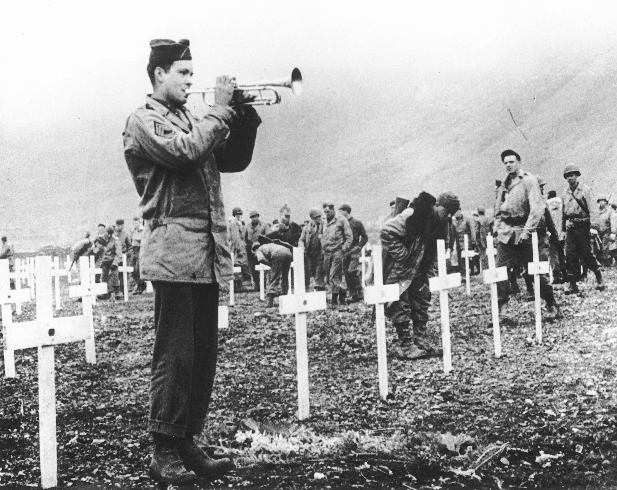 FILE - In this Aug. 1943 file photo, a bugler sounds taps during a memorial service while a group of G.I.s visit the graves of comrades who fell in the reconquest of Attu Island, part of the Aleutian Islands of Alaska. May 30, 2018 will mark the 75th anniversary of American forces recapturing Attu Island in Alaska’s Aleutian chain from Japanese forces. It was the only World War II battle fought on North American soil. (AP Photo, File)