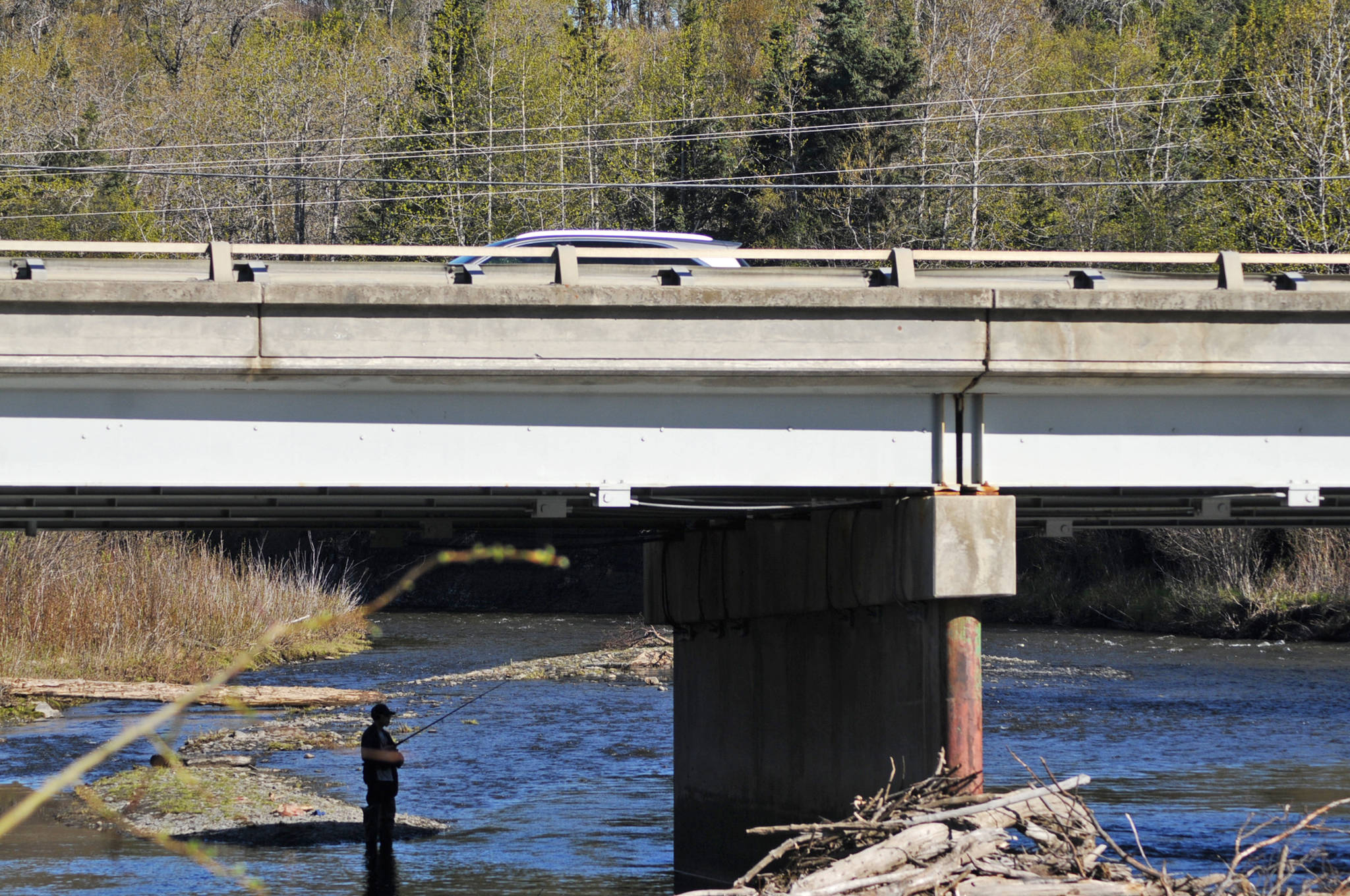 A car passes over the Deep Creek bridge as an angler tosses a line in the water on Sunday, May 28, 2018 in Ninilchik, Alaska. Despite the perfect weather and holiday weekend, few anglers dotted the banks of the Ninlichik River and Deep Creek on Sunday, in part because the number of salmon in the rivers so far is still fairly paltry. The Alaska Department of Fish and Game classified the fishing over Memorial Day weekend as poor, in part because the water temperatures are still chilly for this time of year. (Photo by Elizabeth Earl/Peninsula Clarion)