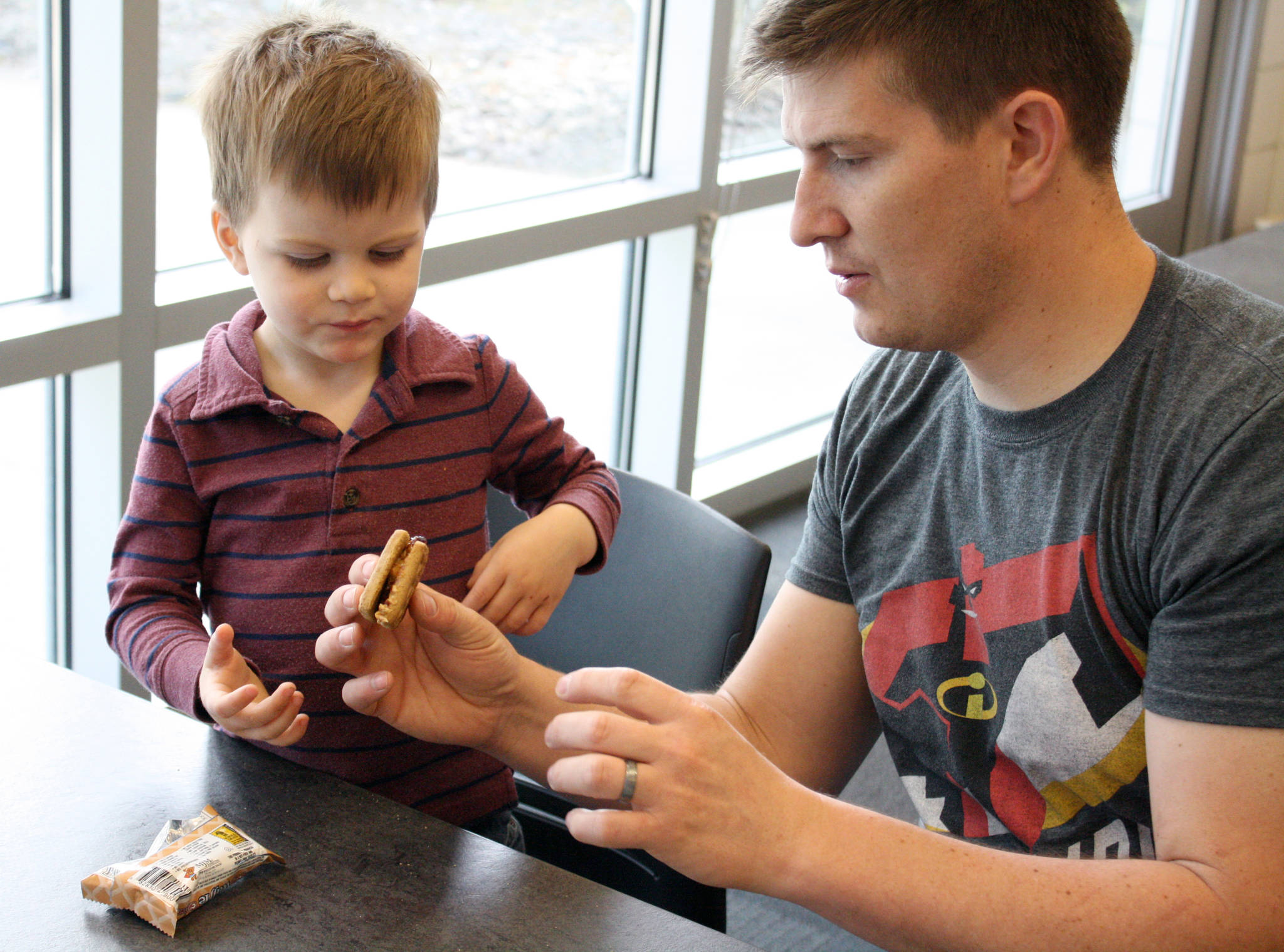 Kyle Downum hands his son a graham cracker sandwich at the Kenai Community Library on Monday. The family took a break from the library’s many activists to enjoy a free afternoon lunch. The Kenai and Soldotna libraries are offering free lunches to children 18 and under as part of its Summer Food Program. (Photo by Erin Thompson/Peninsula Clarion)