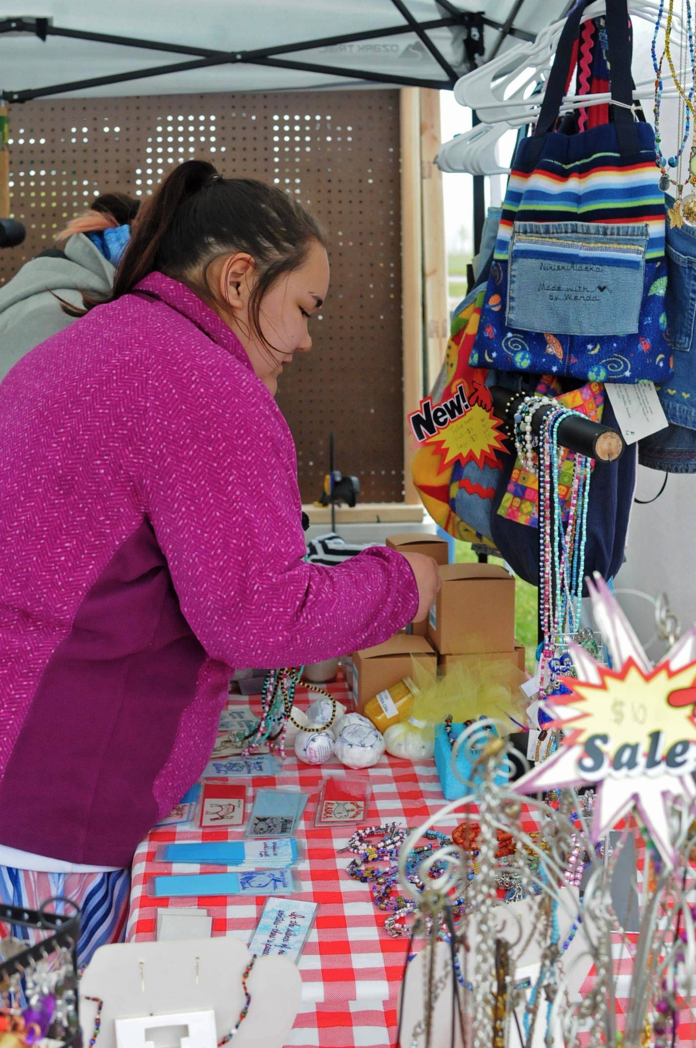 Vanessa Lopez of Nikiski arranges necklaces on a rack at the stall for The Studio at the Kenai Saturday Market on Saturday, June 9, 2018 in Kenai, Alaska. The Kenai Chamber of Commerce coordinates the Saturday markets for farmers and craftspeople on the lawn at the Kenai Visitors and Cultural Center every Saturday during the summer. (Photo by Elizabeth Earl/Peninsula Clarion)