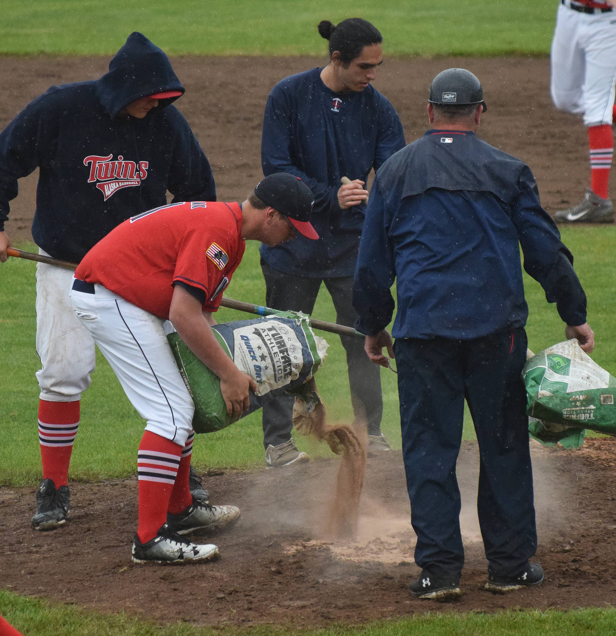 Twins players and coaches drop quick dry soil on the mound at Coral Seymour Memorial Ballpark, on a wet Friday afternoon in Kenai. (Photo by Joey Klecka/Peninsula Clarion)