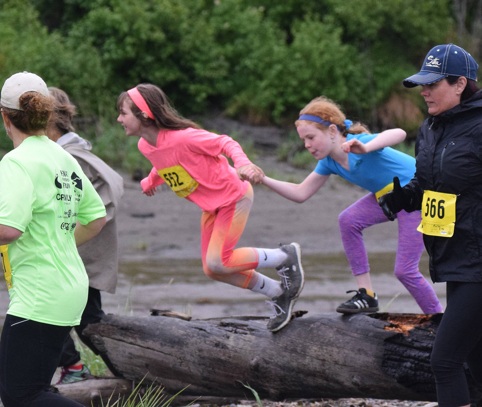 Youth runners Karalyn Viehdeffer (left) and Audrey Hobart Anderson hurdle a log together Saturday at the fourth annual Clam Scramble 5K in Ninilchik. (Photo by Joey Klecka/Peninsula Clarion)
