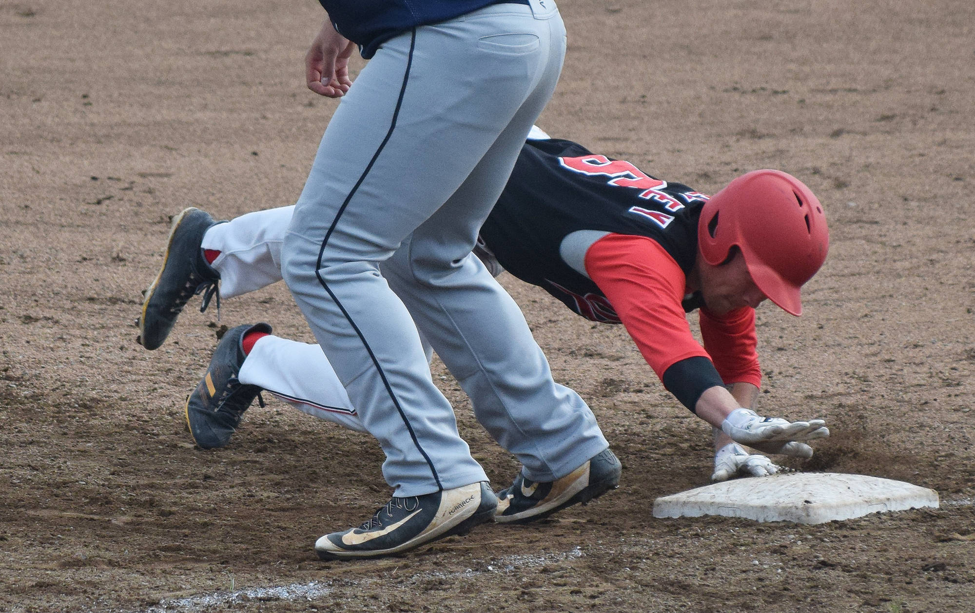 Peninsula Oilers runner Evan Berkey dives back to first ahead of the tag from Chugiak/Eagle River first baseman Nick Kreutzer, Friday night at Coral Seymour Memorial Park in Kenai. (Photo by Joey Klecka/Peninsula Clarion)