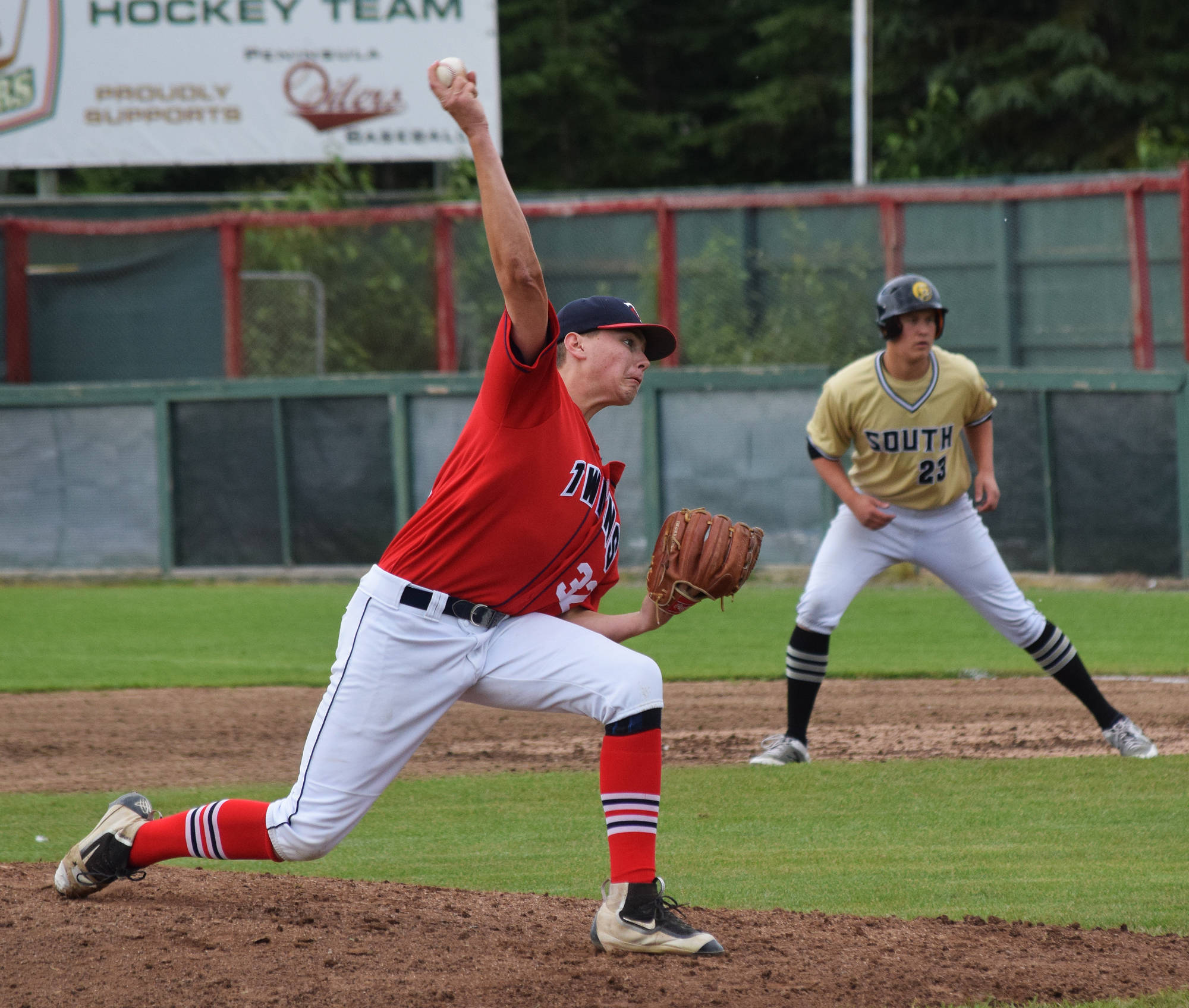 Legion Twins starter Adam Brinster (left) unleashes a pitch with South baserunner Gunnar Nix attempting a steal Wednesday afternoon at Coral Seymour Memorial Ballpark. (Photo by Joey Klecka/Peninsula Clarion)