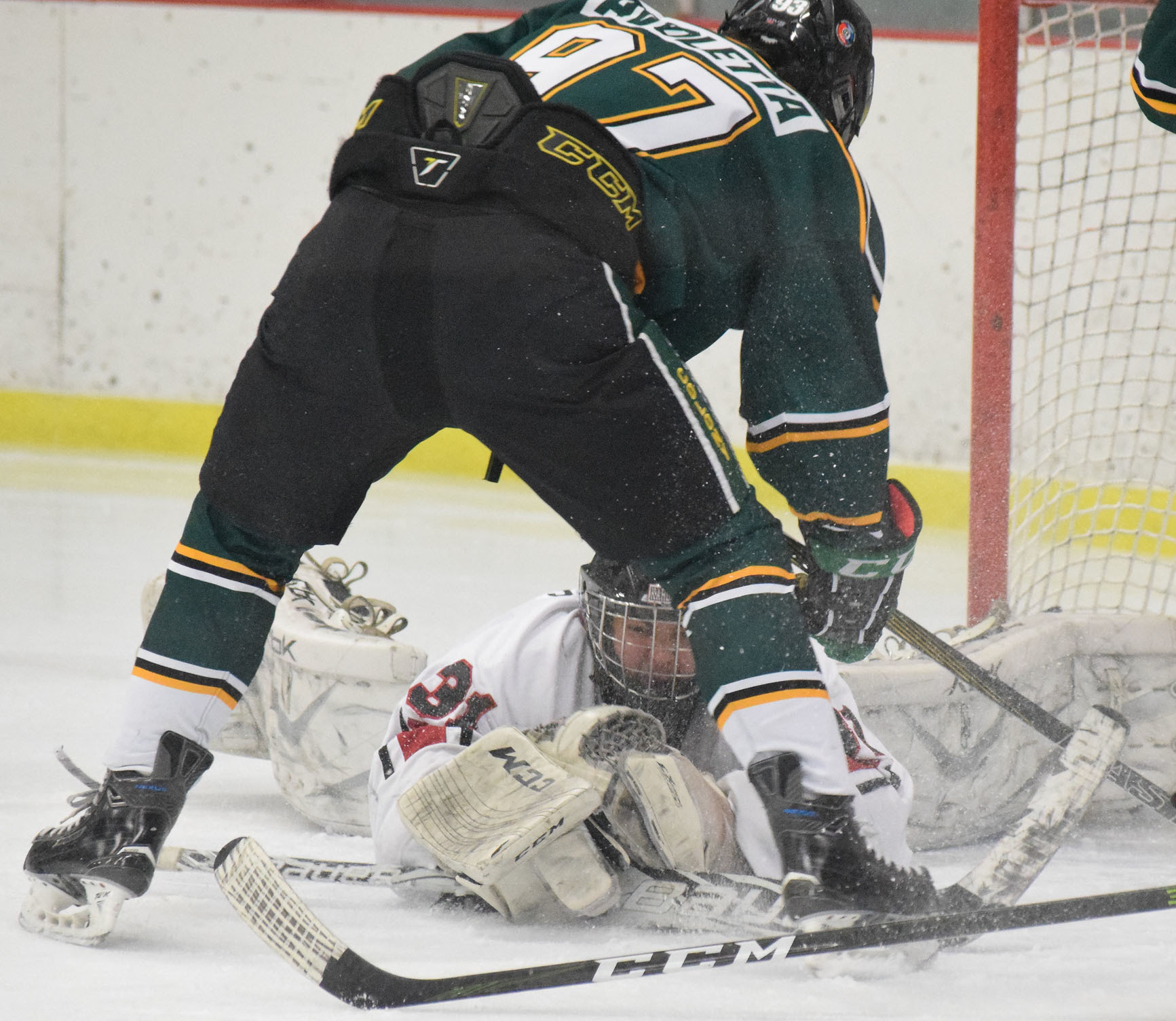 Kenai Kardinals goaltender Ryan Williams sprawls out to catch the puck under Colony forward Tristan Avoletta, Thursday night at the Kenai Multipurpose Facility. (Photo by Joey Klecka/Peninsula Clarion)