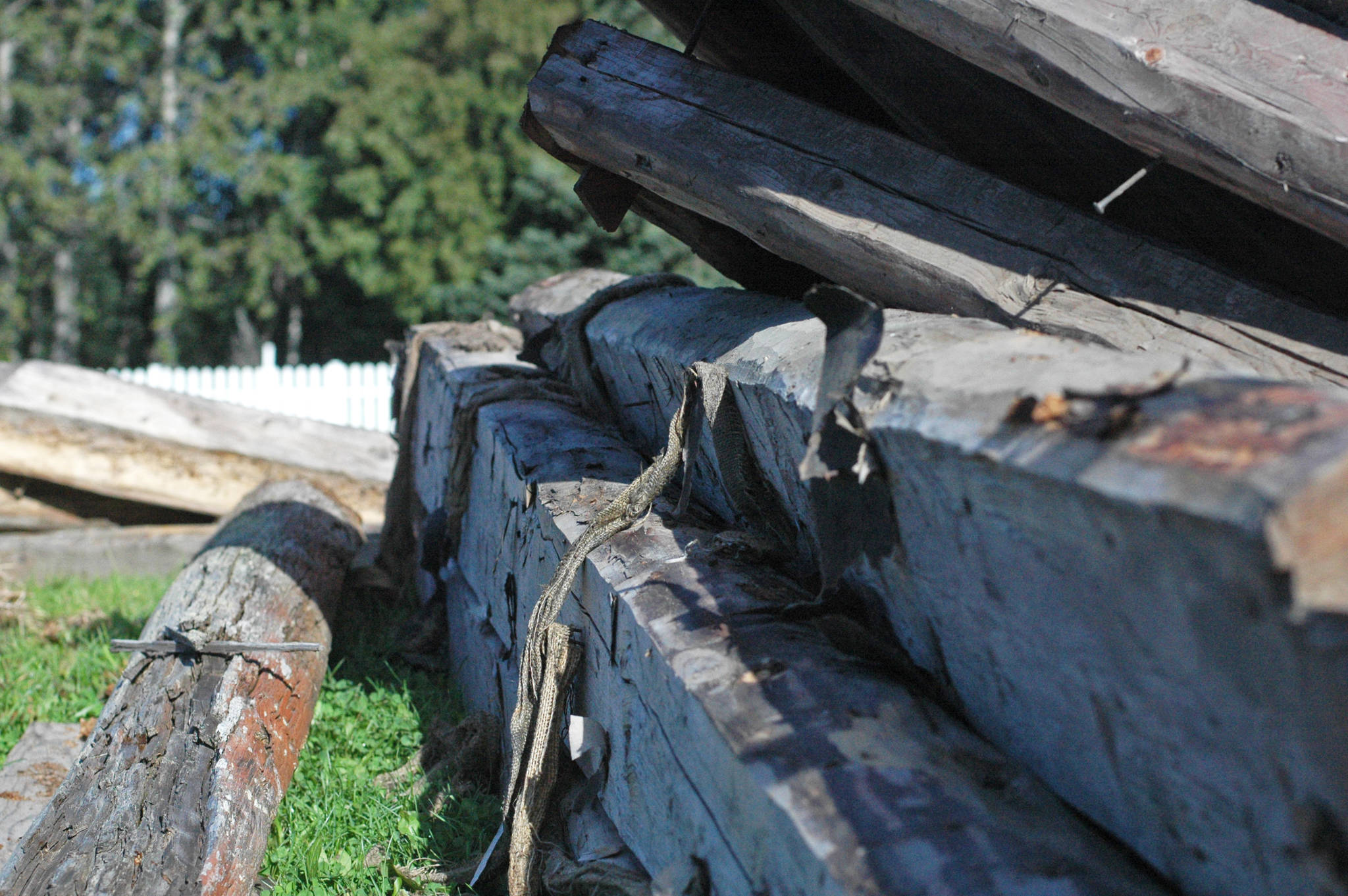 Logs from a deconstructed cabin in Old Town Kenai lie piled beside the work site on Wednesday, Aug. 29, 2018 in Kenai, Alaska. The workers will fill the sunken foundation, place floorboards and then reuse the historic logs to rebuild the cabin, which belonged to Kenai’s first jailer. (Photo by Elizabeth Earl/Peninsula Clarion)