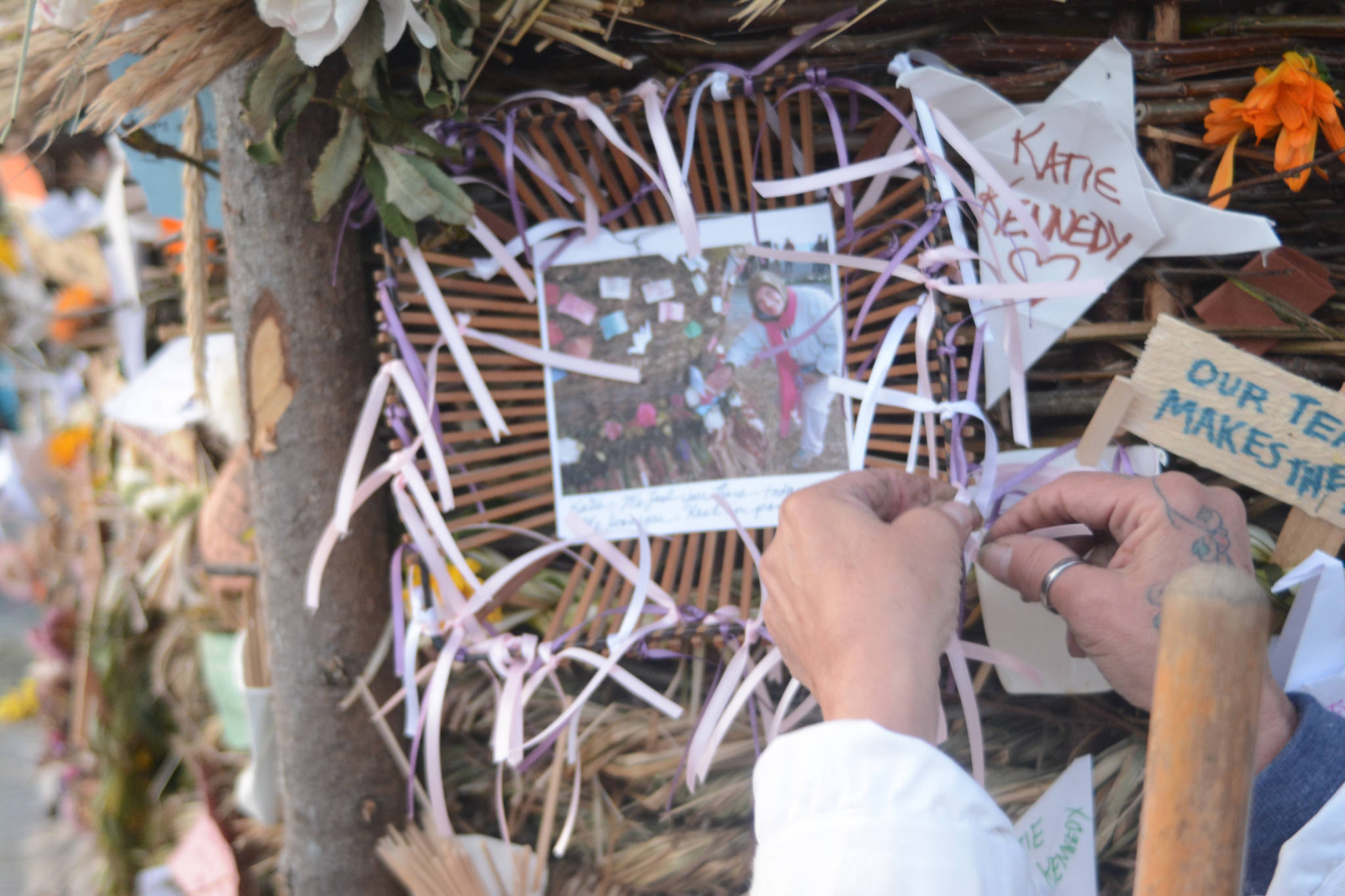 A woman ties a ribbon to a memorial to Katie Kennedy at this year’s Burning Basket, Dream, on Sunday, Sept. 9, 2018 at Mariner Park in Homer, Alaska. The photo shows Kennedy placing her bra in the 2017 Burning Basket. Kennedy died of breast cancer this year. (Photo by Michael Armstrong/Homer News)