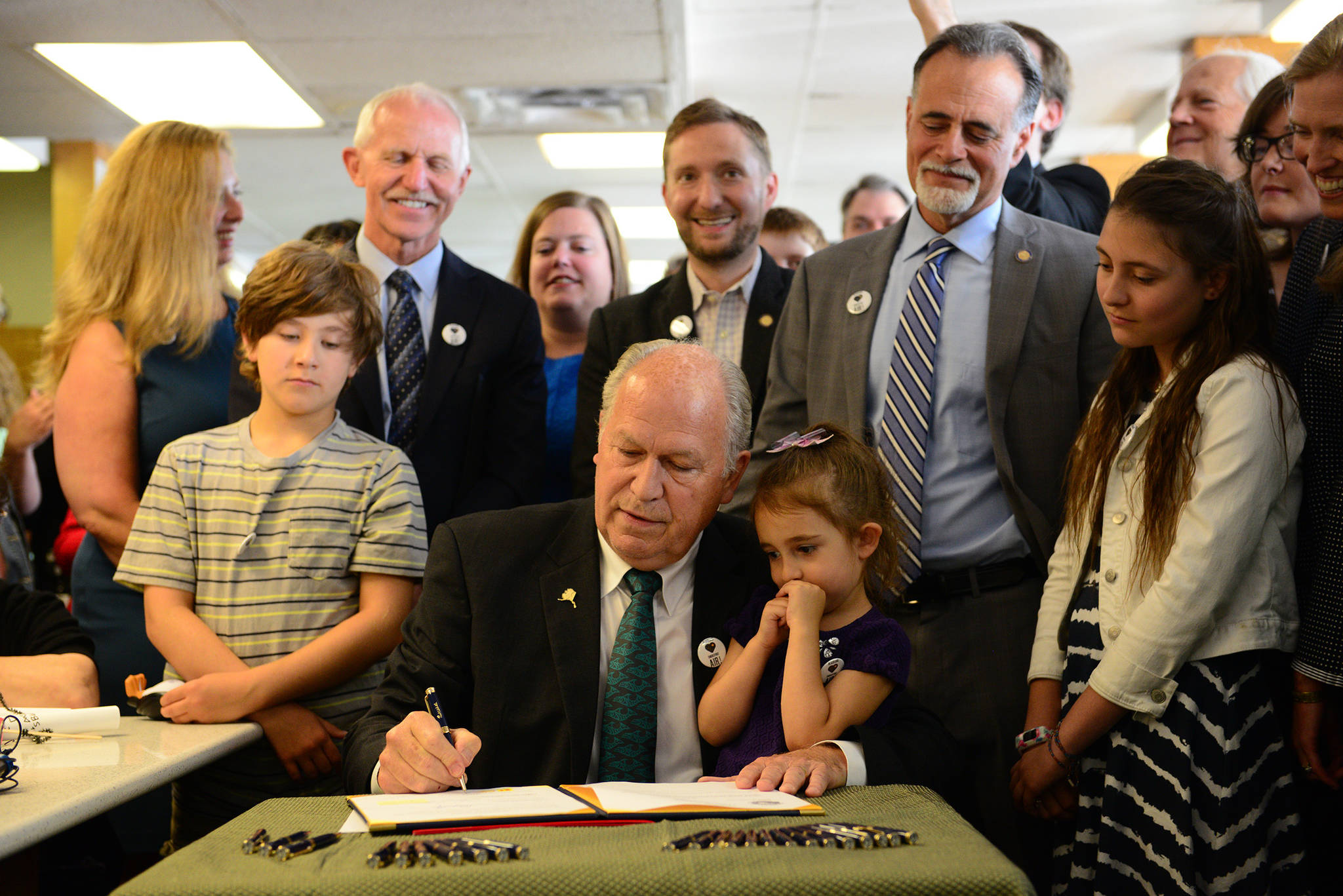In a photo provided by the office of the governor, Gov. Bill Walker signs Senate Bill 63, a statewide public smoking ban, on Tuesday, July 17, 2018, at the Lucky Wishbone restaurant in Anchorage. The law goes into effect on Oct. 1. Standing at right is Sen. Peter Micciche, R-Soldotna, the legislative sponsor of the bill. On Walker’s lap is Stella Micciche, one of Micciche’s daughters. Also visible, from right to left behind Walker are Dr. Jay Butler, Alaska’s chief medical officer; Rep. Geran Tarr, D-Anchorage; Rep. Jason Grenn, I-Anchorage; Micciche; Rep. Chris Birch, R-Anchorage; and the smile of Emily Nenon of the American Cancer Society. (Courtesy photo)