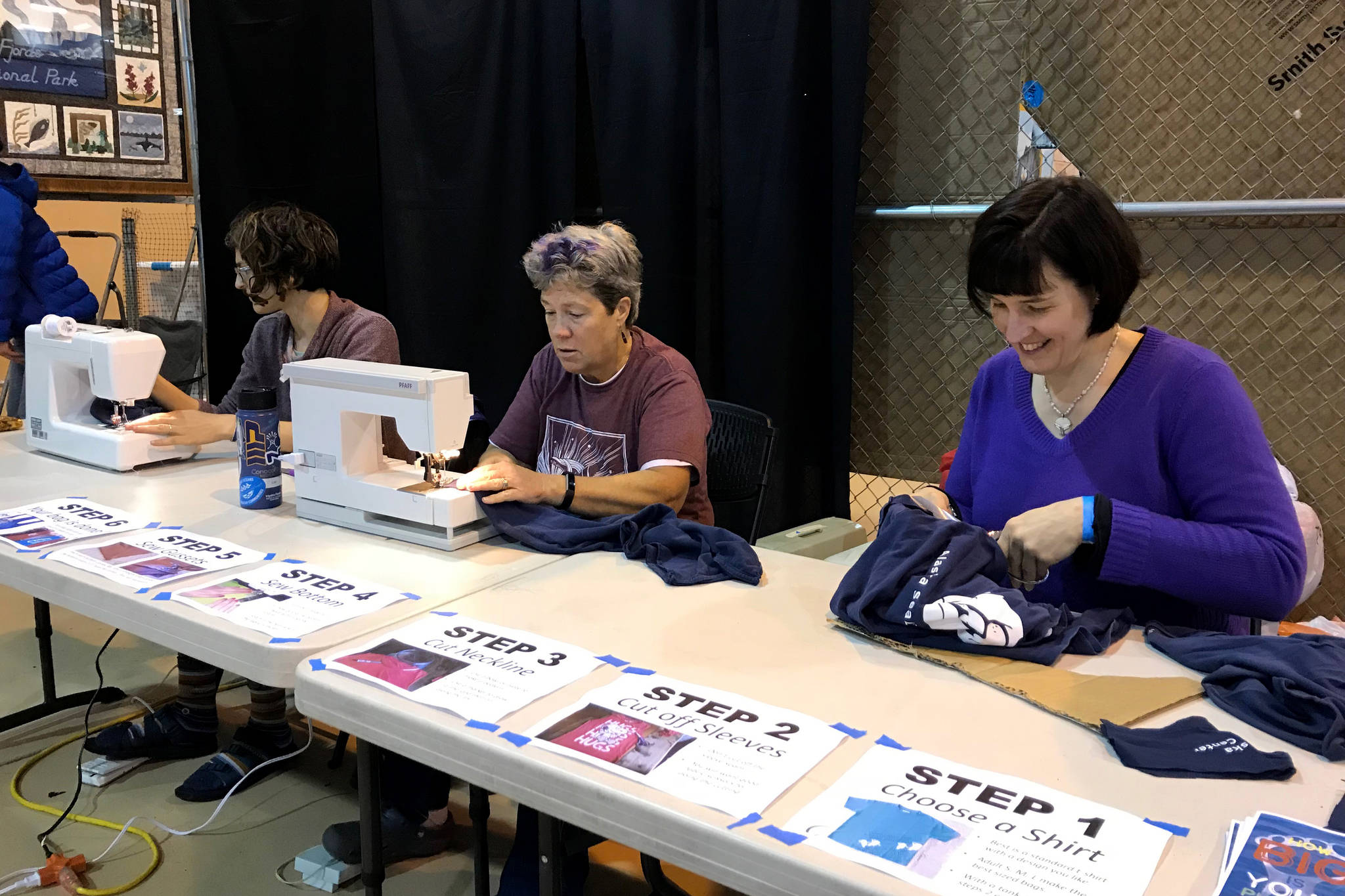 Lori Landstrom, left, and Tara Riemer, right, of Sustainable Seward create reusable shopping bags out of donated shirts during the Seward Music and Arts Festival on Sunday. Sustainable Seward is a grassroots organization working to raise awareness and implement solutions for waste reduction and recycling in the Seward area. (Photo by Kat Sorensen/Peninsula Clarion)