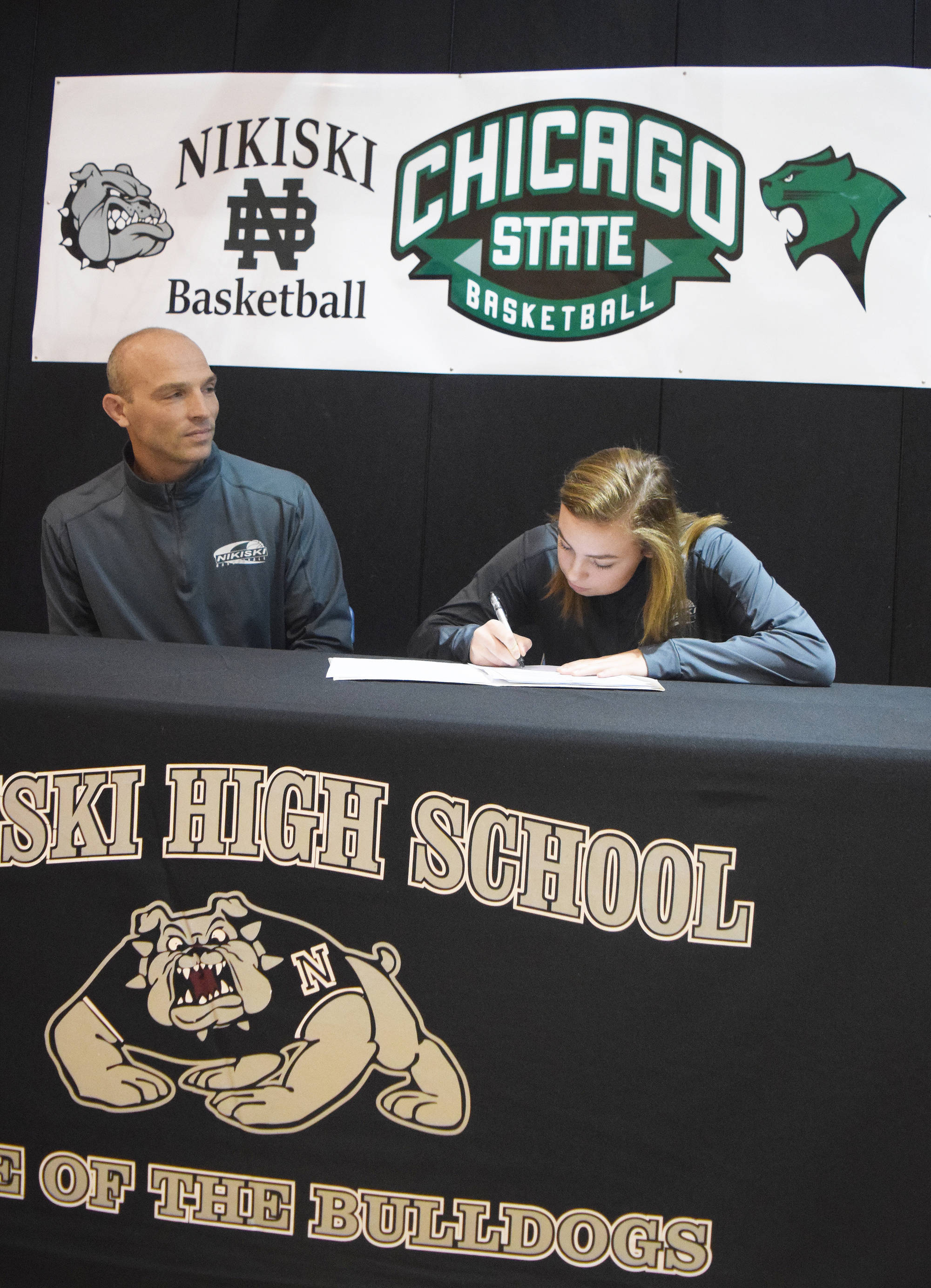 Nikiski senior Bethany Carstens signs her letter of intent, with father Dan Carstens looking on, to play at Division I basketball at Chicago State University in a ceremony Thursday at Nikiski High School. (Photo by Joey Klecka/Peninsula Clarion)