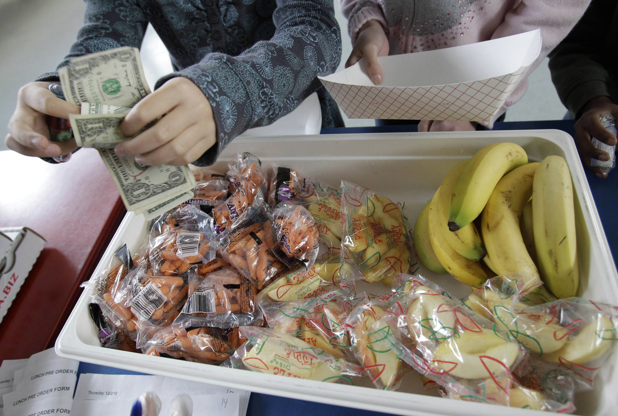 FILE – In this Dec. 2, 2010, file photo, a child pays for a lunch consisting of fruits and vegetables during a school lunch program at Fairmeadow Elementary School in Palo Alto, Calif. California and Pennsylvania both passed laws in 2017 to outlaw "lunch shaming" of children for unpaid meals, with the Pennsylvania measure that became law in November requiring communication about money owed on meal accounts to be done between school officials and parents, and not involve the student. (AP Photo/Paul Sakuma, File)