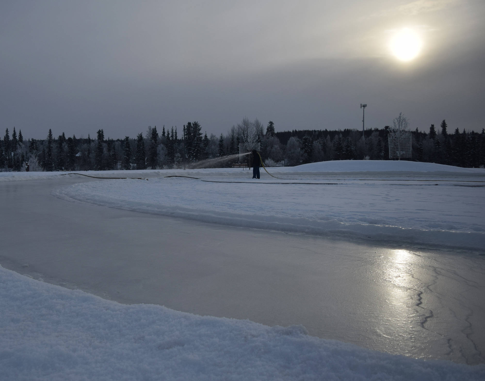 A Soldotna Parks & Recreation worker sprays a layer of water to be frozen into a skating rink Thursday at Soldotna Creek Park. (Photo by Joey Klecka/Peninsula Clarion)