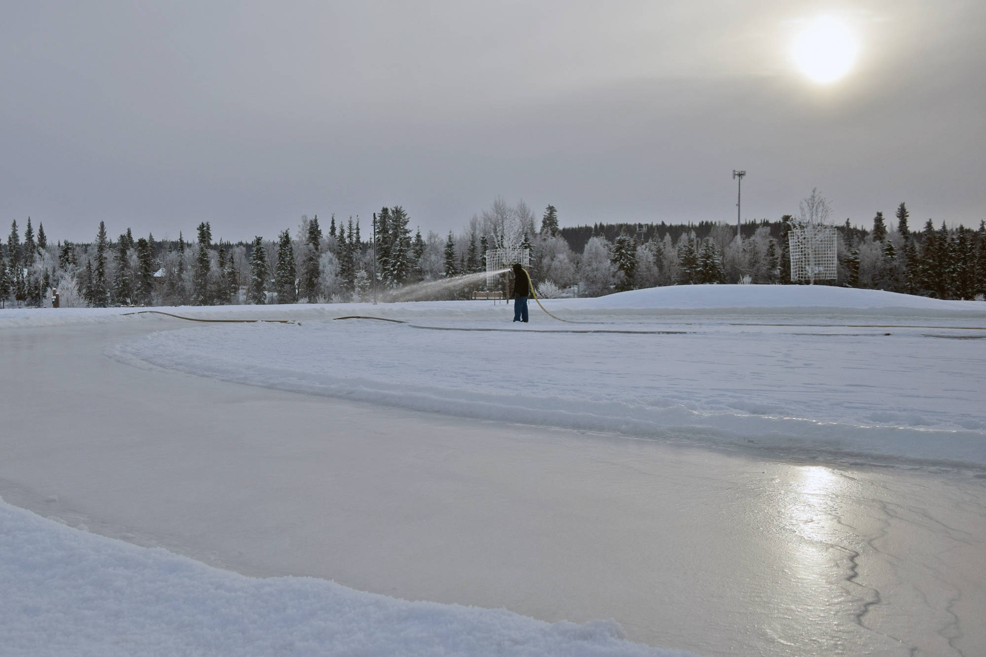 A Soldotna Parks & Recreation worker sprays a layer of water to be frozen into a skating rink in 2018 at Soldotna Creek Park. (Photo by Joey Klecka/Peninsula Clarion)