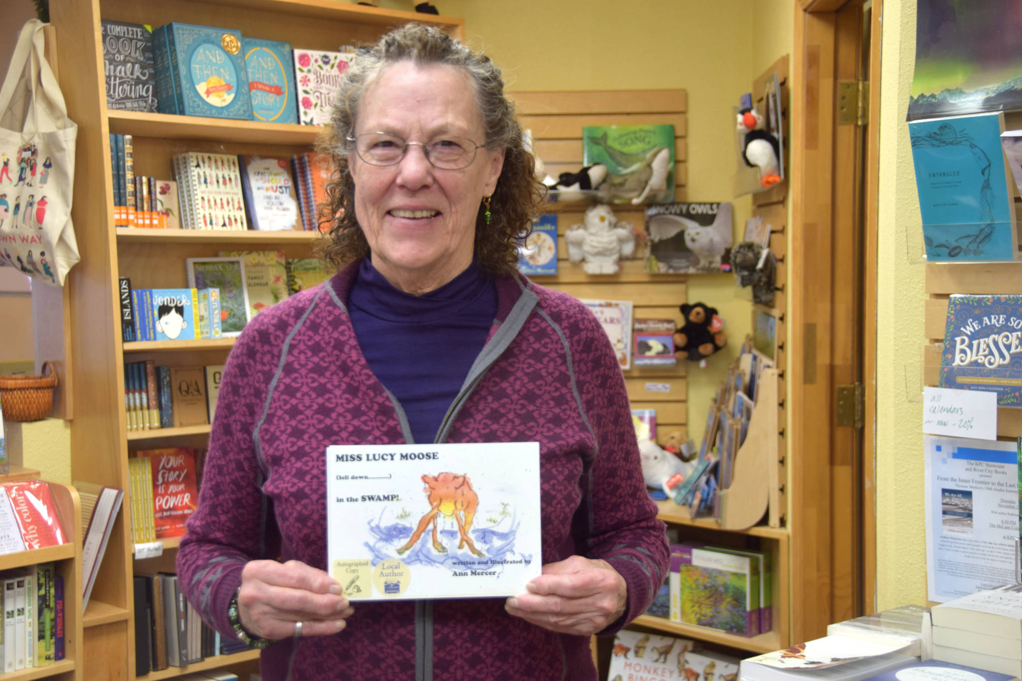 Local author Ann Mercer poses with her book, “Miss Lucy Moose Falls Down in the Swamp” at River City Books in Soldotna on Wednesday. (Photo by Brian Mazurek/Peninsula Clarion)