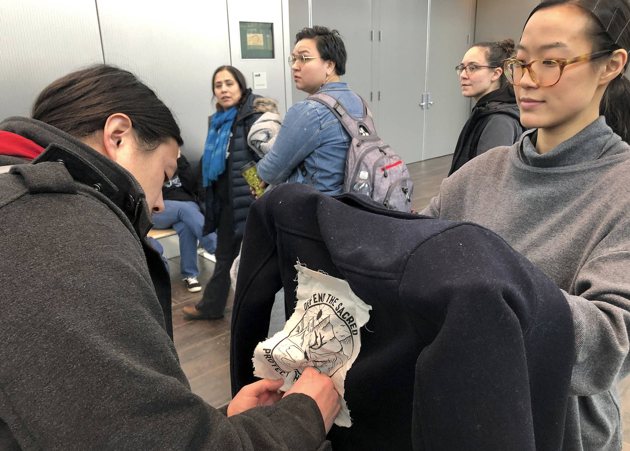Jeff Chen, left, affixes a “Defend the Sacred” logo to Su Chon’s jacket ahead of a Bureau of Land Management hearing Monday, Feb. 11, 2019, in Anchorage, Alaska. The two Anchorage residents planned to oppose drilling as the federal agency accepted public comments on a draft environmental review on drilling within the coastal plain of the Arctic National Wildlife Refuge. (AP Photo/Mark Thiessen)
