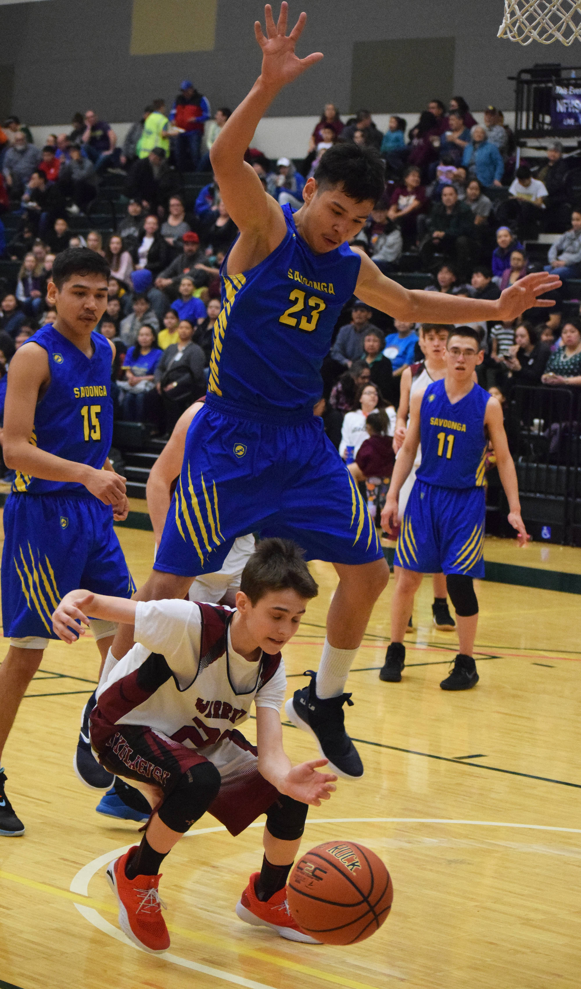 Nikolaevsk’s Lukah Kalugin ducks under the block of Savoonga’s Derek Seppilu (23) Friday at the Class 1A state tournament at the Alaska Airlines Center in Anchorage. (Photo by Joey Klecka/Peninsula Clarion)