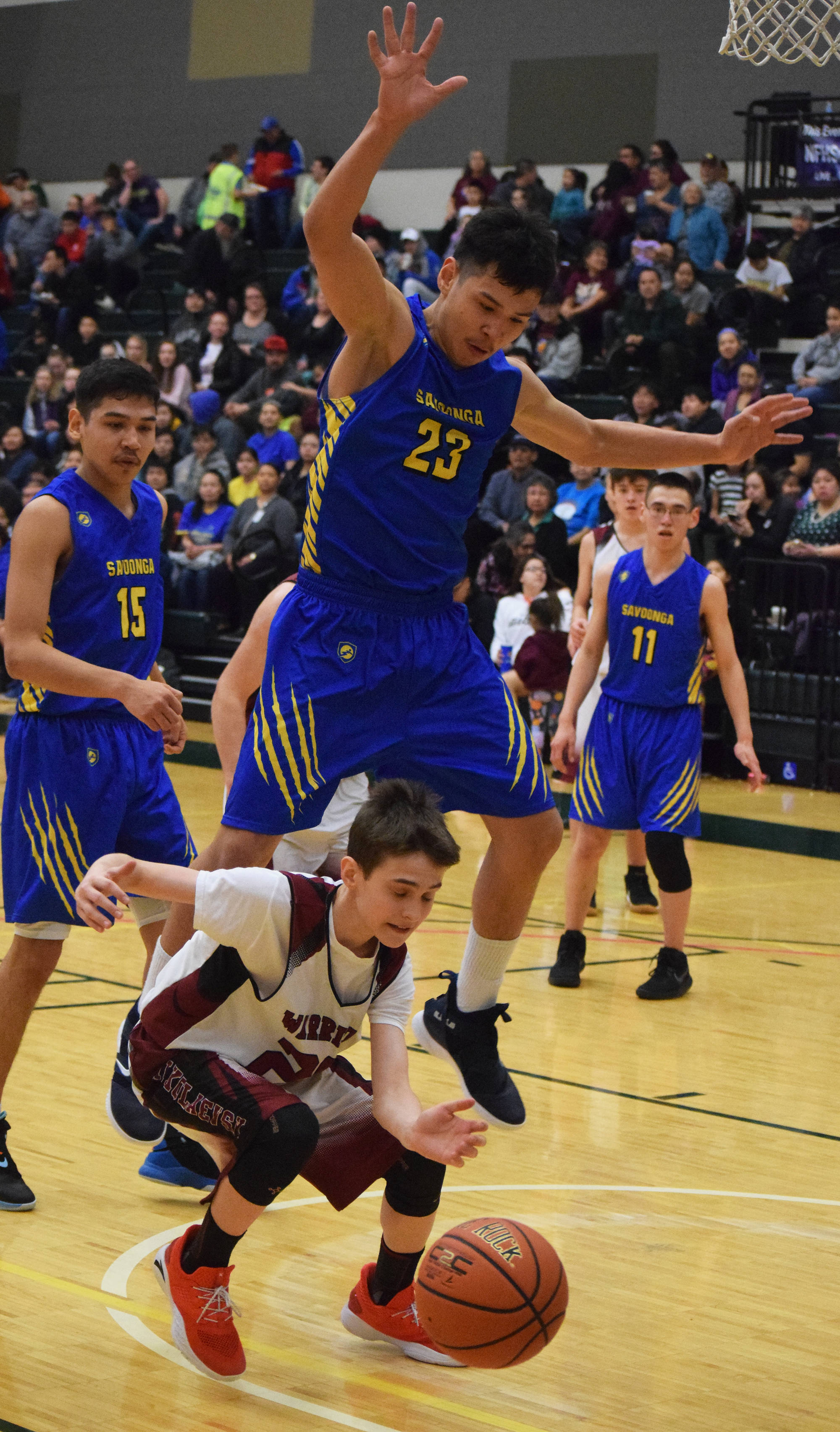 Nikolaevsk’s Lukah Kalugin ducks under the block of Savoonga’s Derek Seppilu (23) Friday at the Class 1A state tournament at the Alaska Airlines Center in Anchorage. (Photo by Joey Klecka/Peninsula Clarion)
