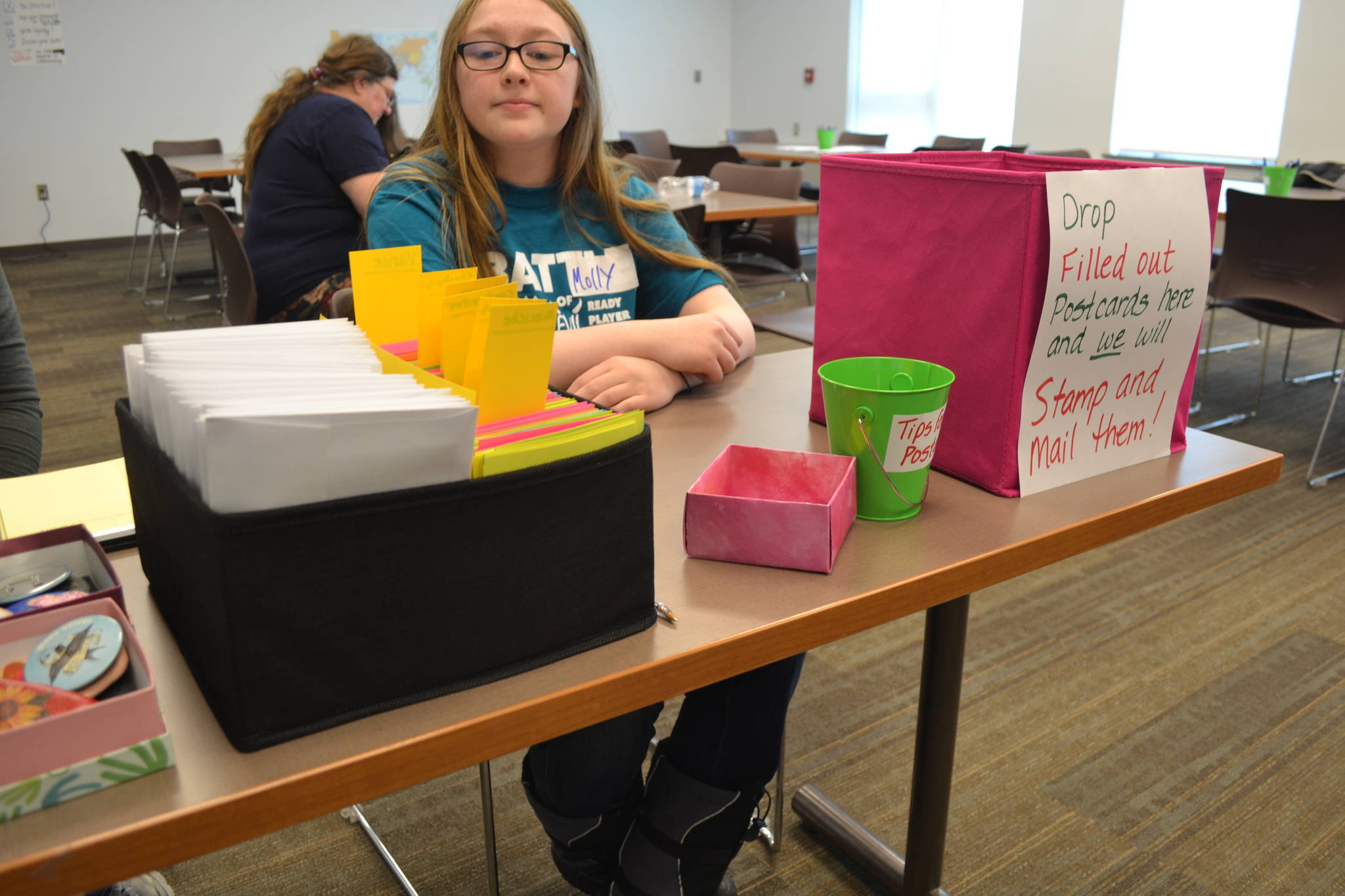 River City Academy student Molly Koski helps host a postcard-writing event that encourages students and community members to reach out to their local lawmakers in regards to Gov. Mike Dunleavy’s recently proposed budget cuts, on Wednesday, March 20, 2019, at the Soldotna Public Library in Soldotna, Alaska. (Photo by Victoria Petersen/Peninsula Clarion)