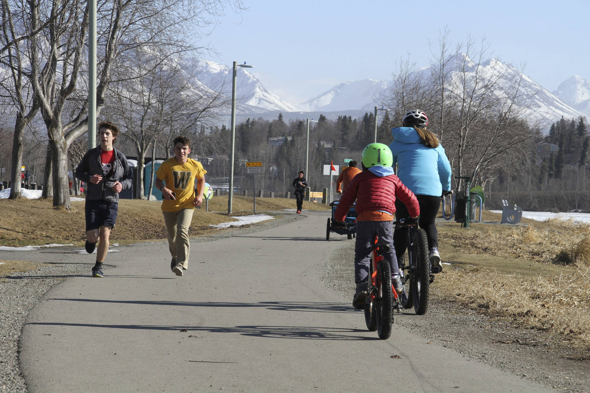 This April 3, 2019, photo shows people running and biking at Westchester Lagoon in Anchorage, Alaska, with the snow-covered Chugach Mountains in the distance. Much of Anchorage’s snow disappeared as Alaska experienced unseasonably warm weather in March. (AP Photo/Mark Thiessen)