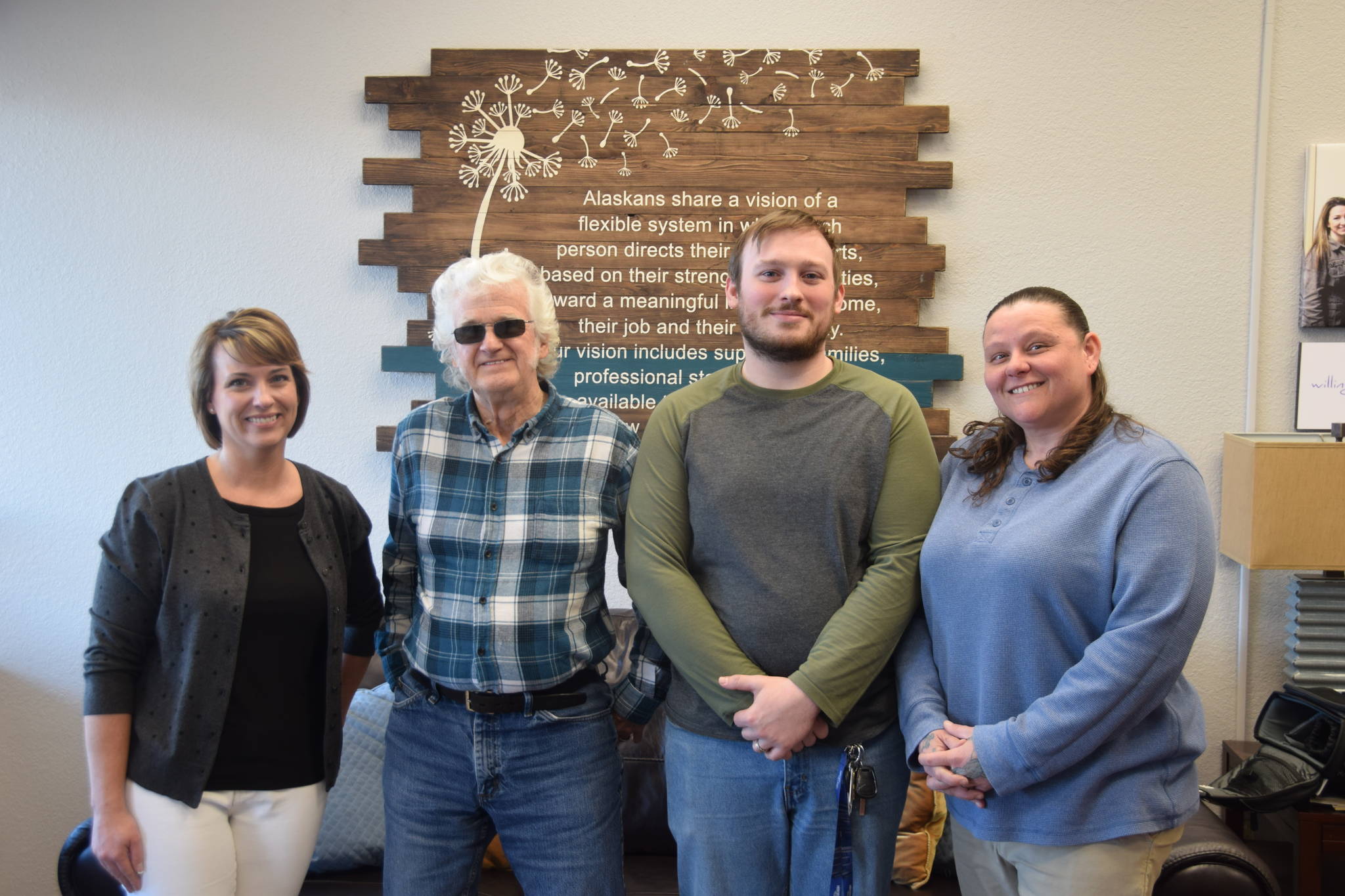 From left to right, Amanda Faulkner, Ron Paul, Troy Bailey and Nikki Marcano of Frontier Community Services stand in front of Frontier’s mission statement on Monday. (Photo by Brian Mazurek/Peninsula Clarion)