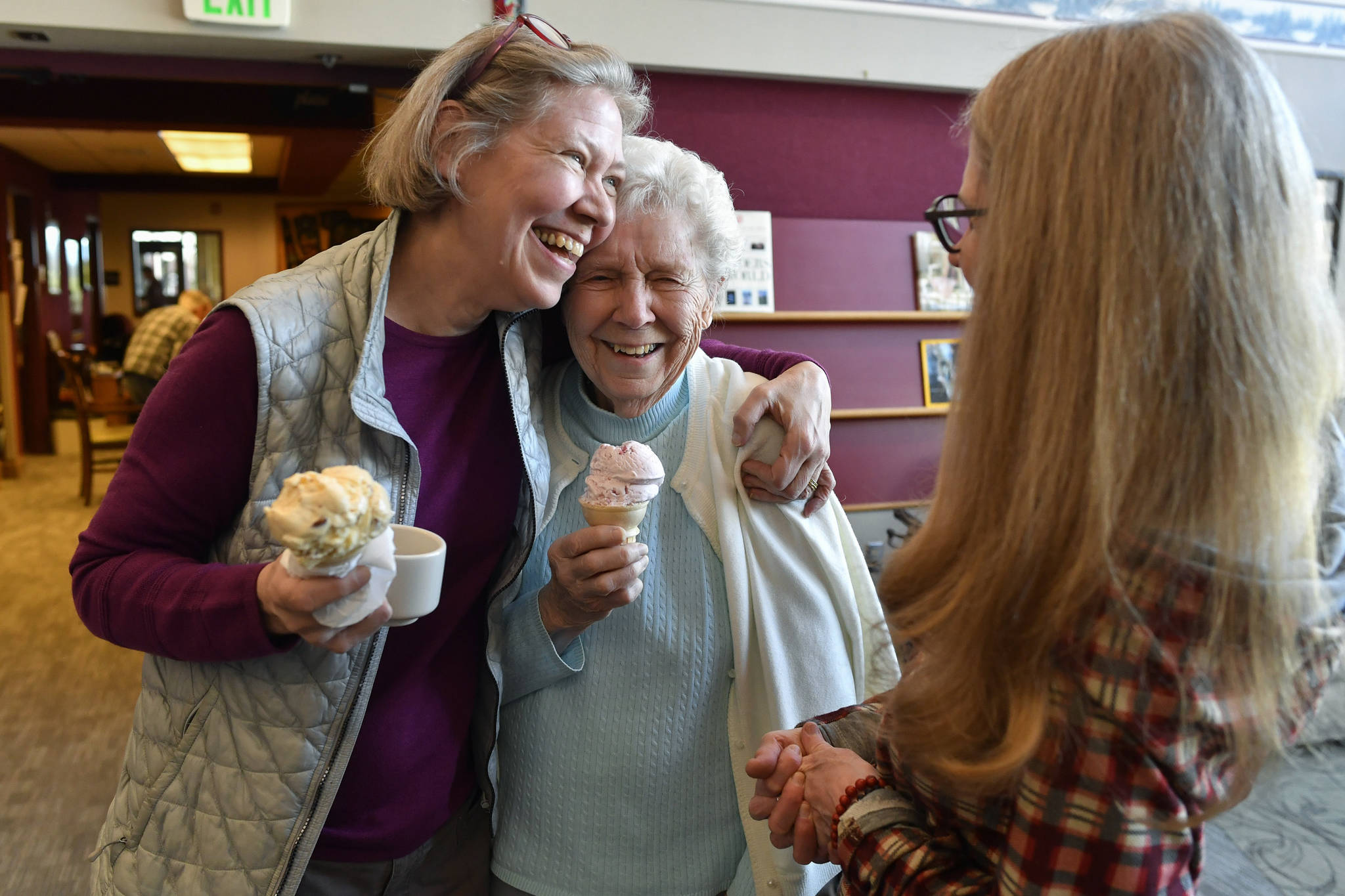 In this March 8, 2019 photo, Margie Beedle, left, hugs her mother, Sally Thibodeau, as they chat with Alaska Pioneer Home employee Laura Minne during the home’s weekly ice cream social. (Michael Penn | Juneau Empire File)