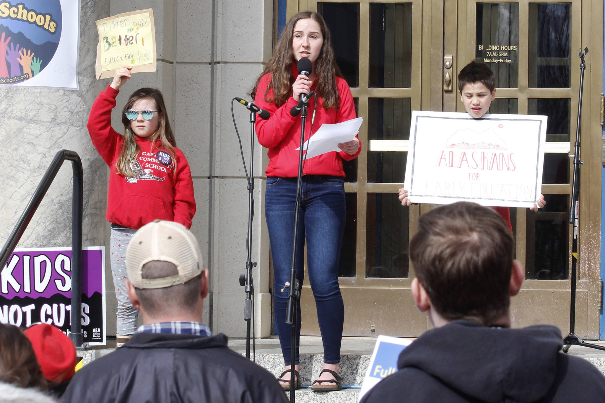 Flanked by younger students holding signs, Juneau-Douglas High School junior Katie McKenna speaks at the Fund Our Future rally on the steps of the Alaska State Capitol on Saturday. (Alex McCarthy | Juneau Empire)
