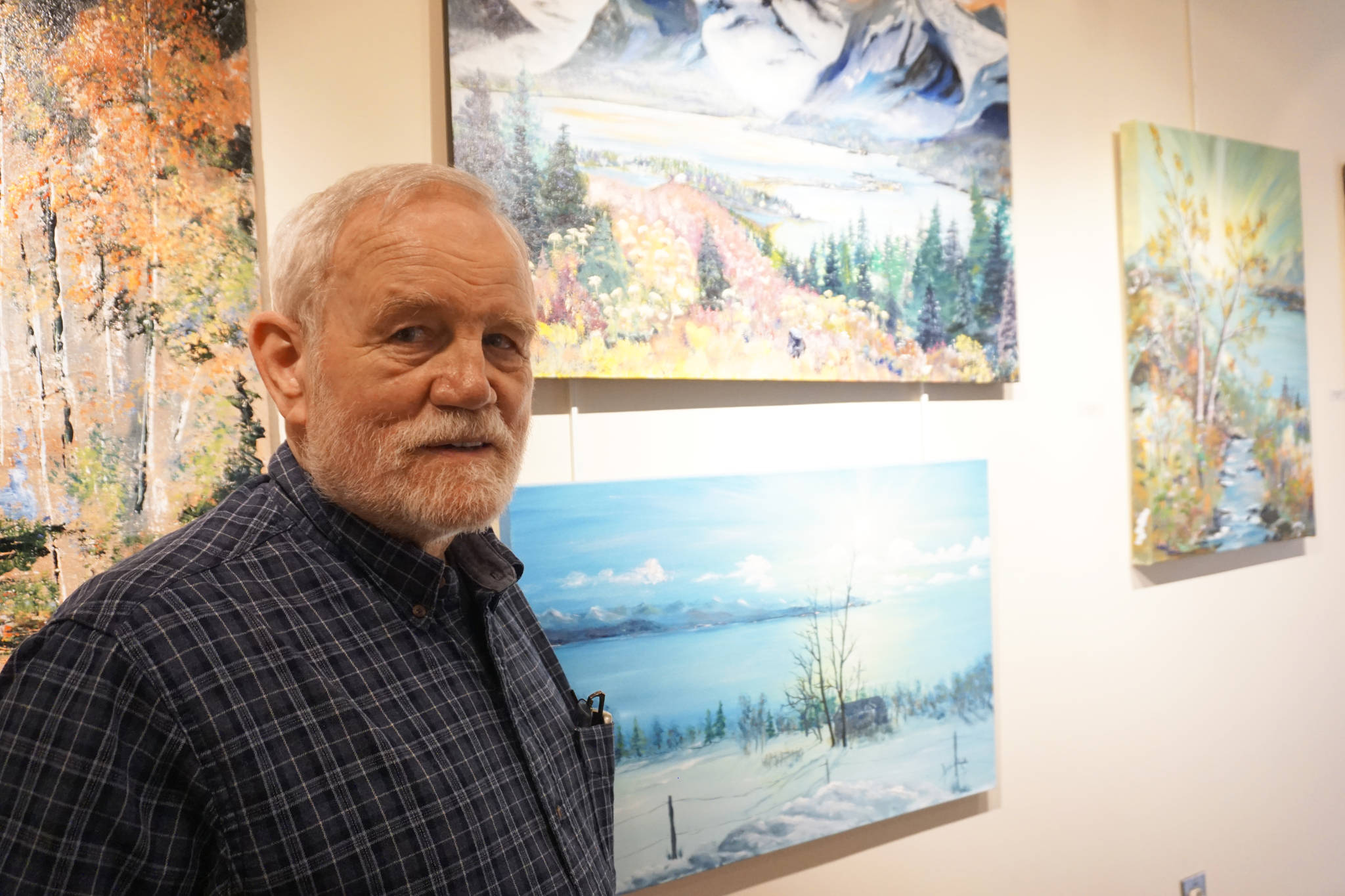 Bill Smith stands by a John Fenske painting, top, that his children bought for him. Fenske’s retrospective show opened on First Friday, April 5, 2019, at Kachemak Bay Campus in Homer, Alaska. (Photo by Michael Armstrong/Homer News)