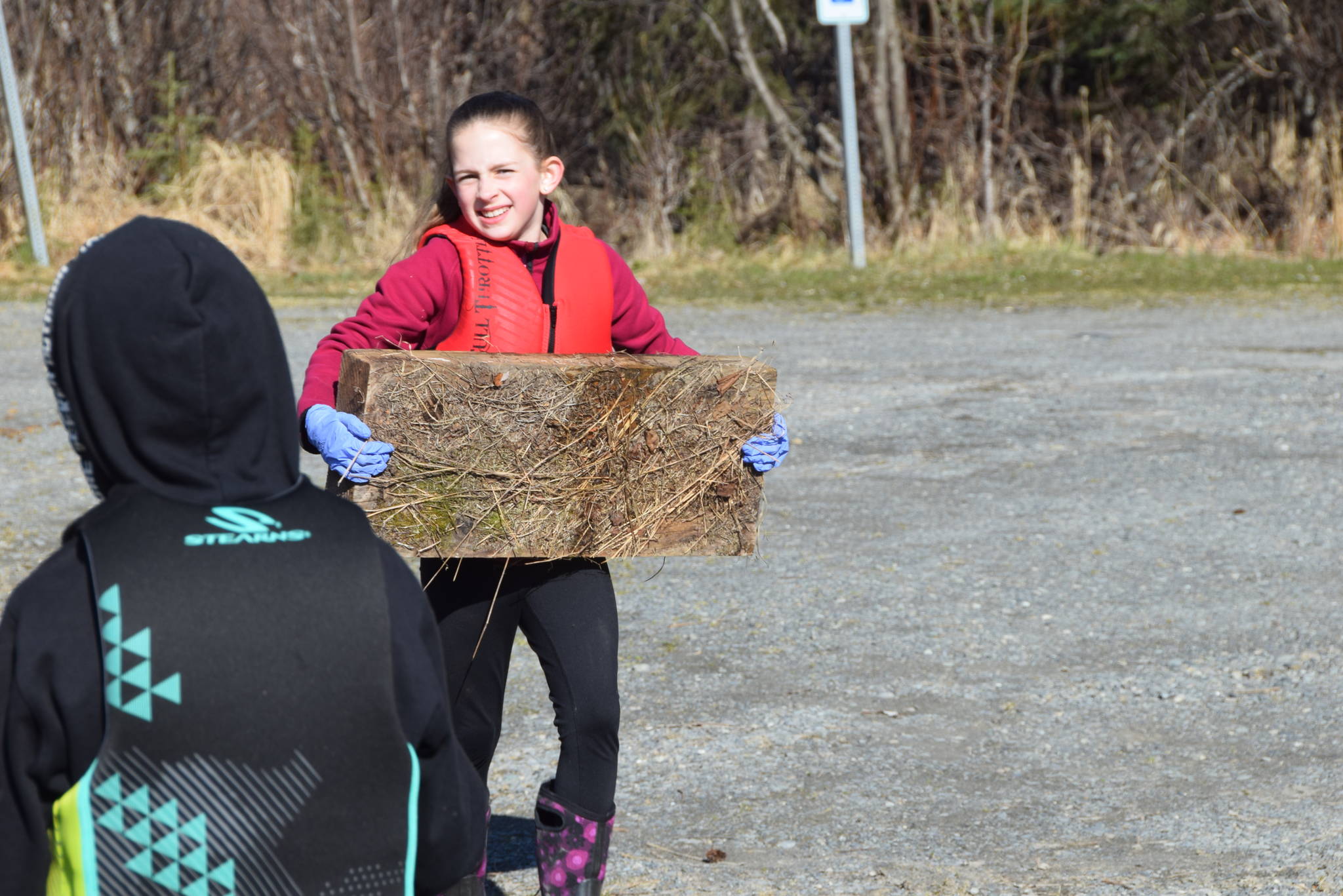 A Redoubt Elementary student carries a piece of wood to the trash pile during the 6th Annual Kids Kenai River Spring Cleanup at Swiftwater Park in Soldotna, Alaska on May 3, 2019. (Photo by Brian Mazurek/Peninsula Clarion)