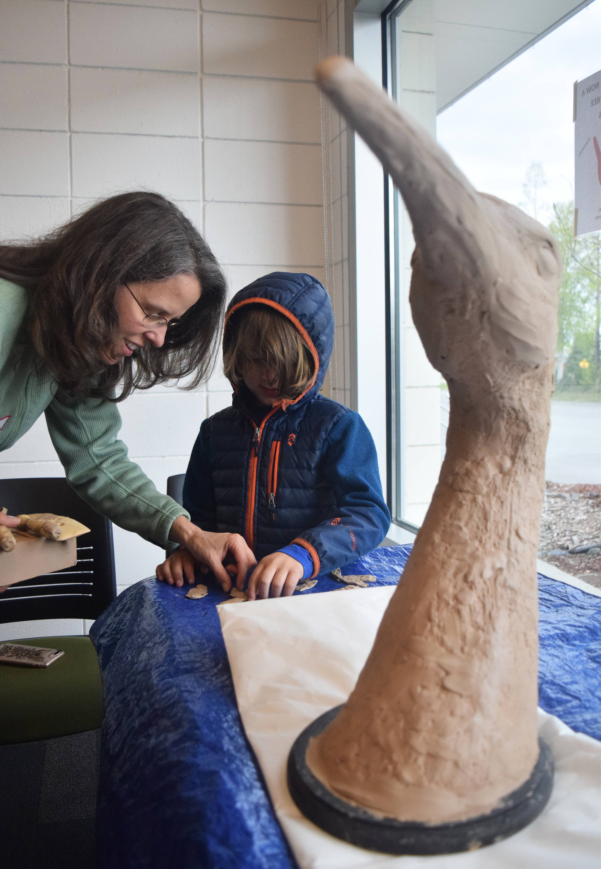 Local artist Christina Demetro helps a young artist create new pieces of clay that will be added to a sculpture of a 6-foot tall sandhill crane on Saturday morning at the Kenai Community Library. The sculpture will ultimately be displayed at the Shimai Toshi Garden Trails, a Japanese Garden that will be the first of its kind in Alaska. The clay sculpture received a local flair as interested artists could choose to add their own style to the statue, which sat in several pieces at the library. The statue will eventually be pieced together and bronzed. (Photo by Joey Klecka/Peninsula Clarion)