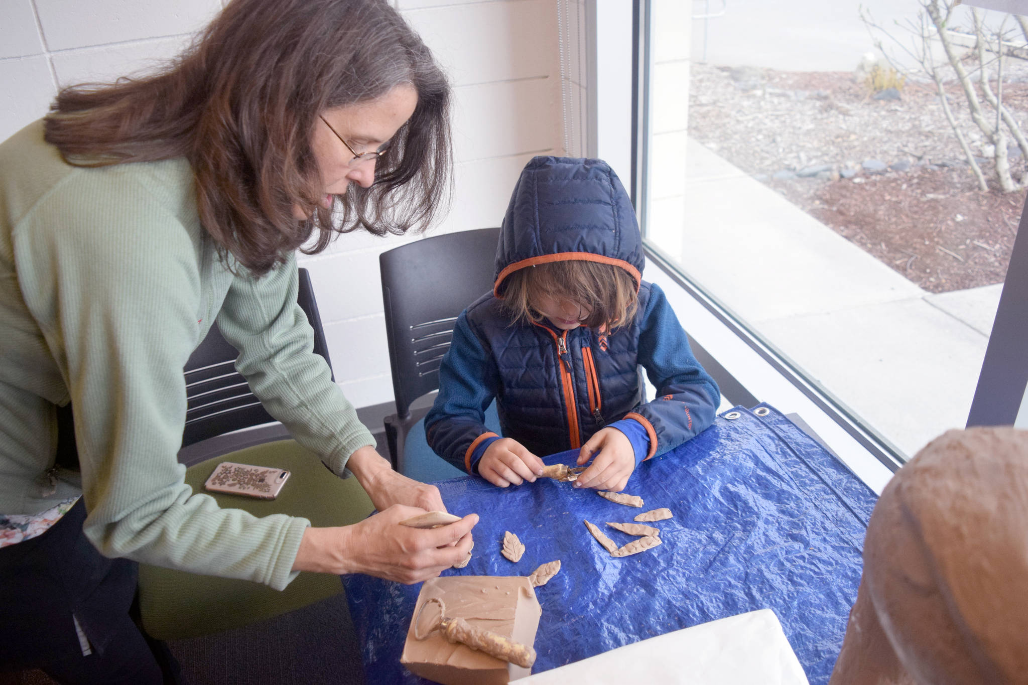 Local artist Christina Demetro helps a young artist create new pieces of clay that will be added to a sculpture of a 6-foot tall sandhill crane on Saturday morning at the Kenai Community Library. The sculpture will ultimately be displayed at the Shimai Toshi Garden Trails, a Japanese Garden that will be the first of its kind in Alaska. The clay sculpture received a local flair as interested artists could choose to add their own style to the statue, which sat in several pieces at the library. The statue will eventually be pieced together and bronzed. (Photo by Joey Klecka/Peninsula Clarion)