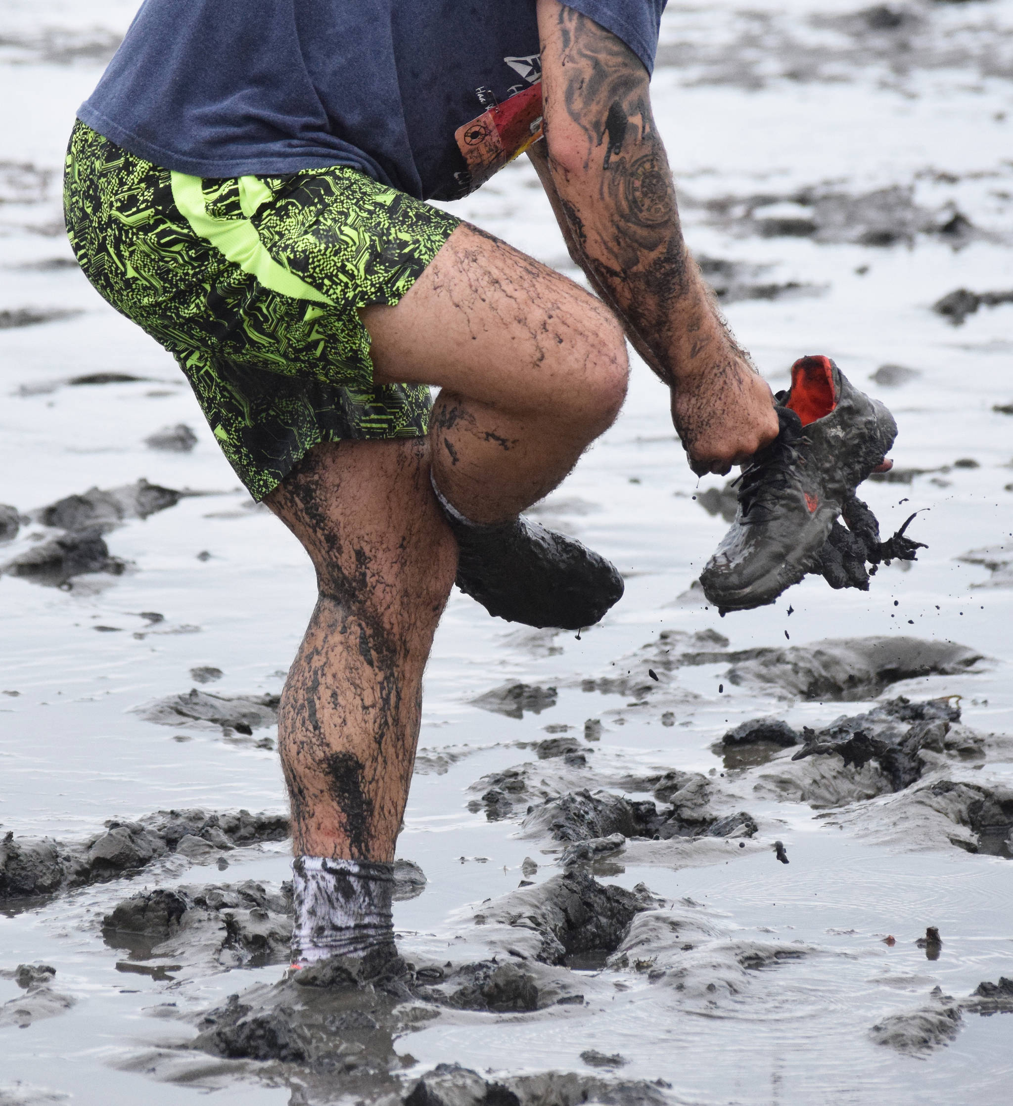 Jay Harris stops to put his shoe back on after it came off in deep mud Saturday at the Ninilchik Clam Scramble Mud and Obstacle Run in Ninilchik, Alaska. (Photo by Joey Klecka/Peninsula Clarion)