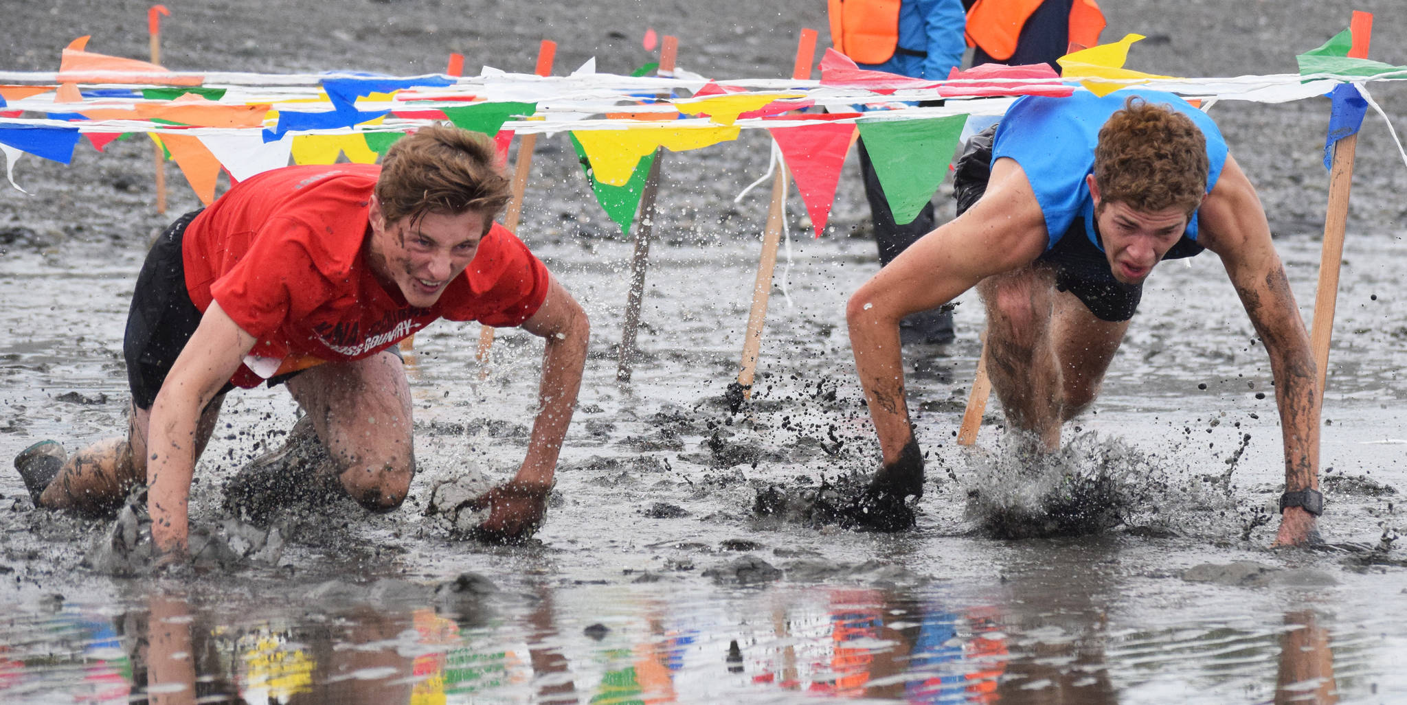 Race leaders Maison Dunham (left) and Aaron Swedberg crawl through the mud Saturday, June 15, 2019, at the Ninilchik Clam Scramble Mud and Obstacle Run in Ninilchik, Alaska. (Photo by Joey Klecka/Peninsula Clarion)