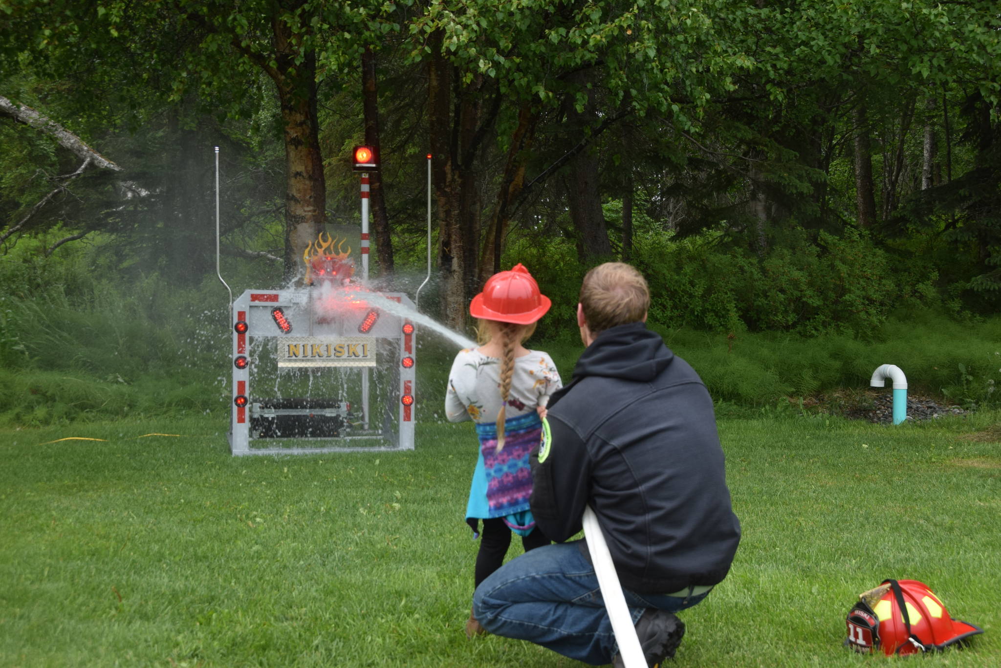 Tyler Smith with the Nikiski Fire Department helps Jenasis Dempster blast a target with a fire hose during the Family Fun in the Midnight Sun festival at the North Peninsula Recreation Center in Nikiski, Alaska on June 15, 2019. (Photo by Brian Mazurek/Peninsula Clarion)