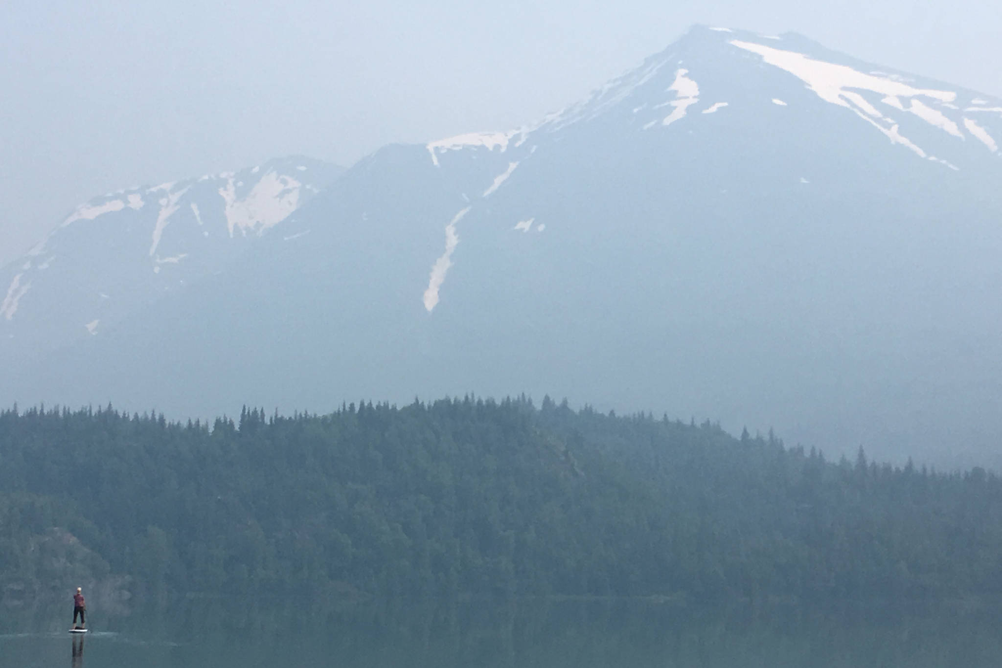 A standup paddleboarder braves smoky conditions on Lower Trail Lake on Wednesday, June 26, 2019, near Moose Pass, Alaska. Smoky conditions persisted throughout the Kenai Peninsula due to the Swan Lake Fire burning north of the Sterling Highway. (Photo by Jeff Helminiak/Peninsula Clarion)