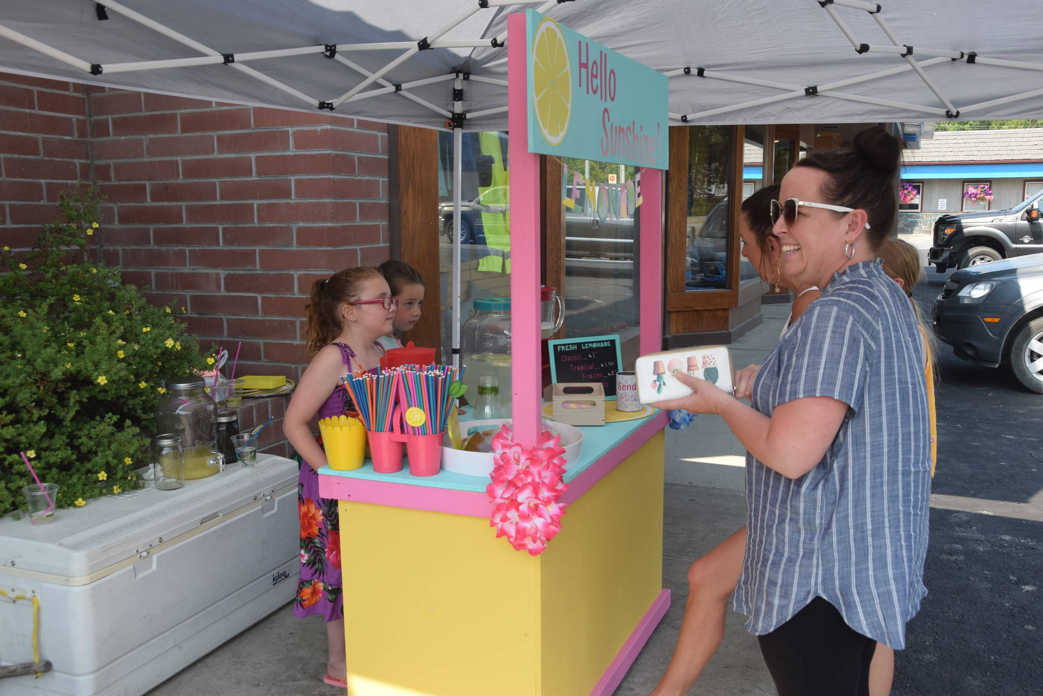 Kinley Clack, left, and Brooklynne Timm serve some customers at their lemonade stand outside of Sweeney’s during Lemonade Day in Soldotna, Alaska on June 29, 2019. (Photo by Brian Mazurek/Peninsula Clarion)